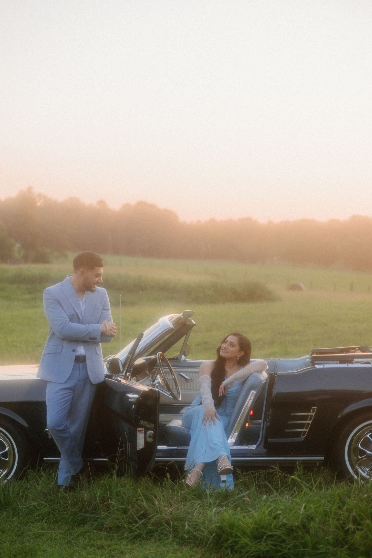 Classic vintage convertible car parked in a grassy field at sunset.