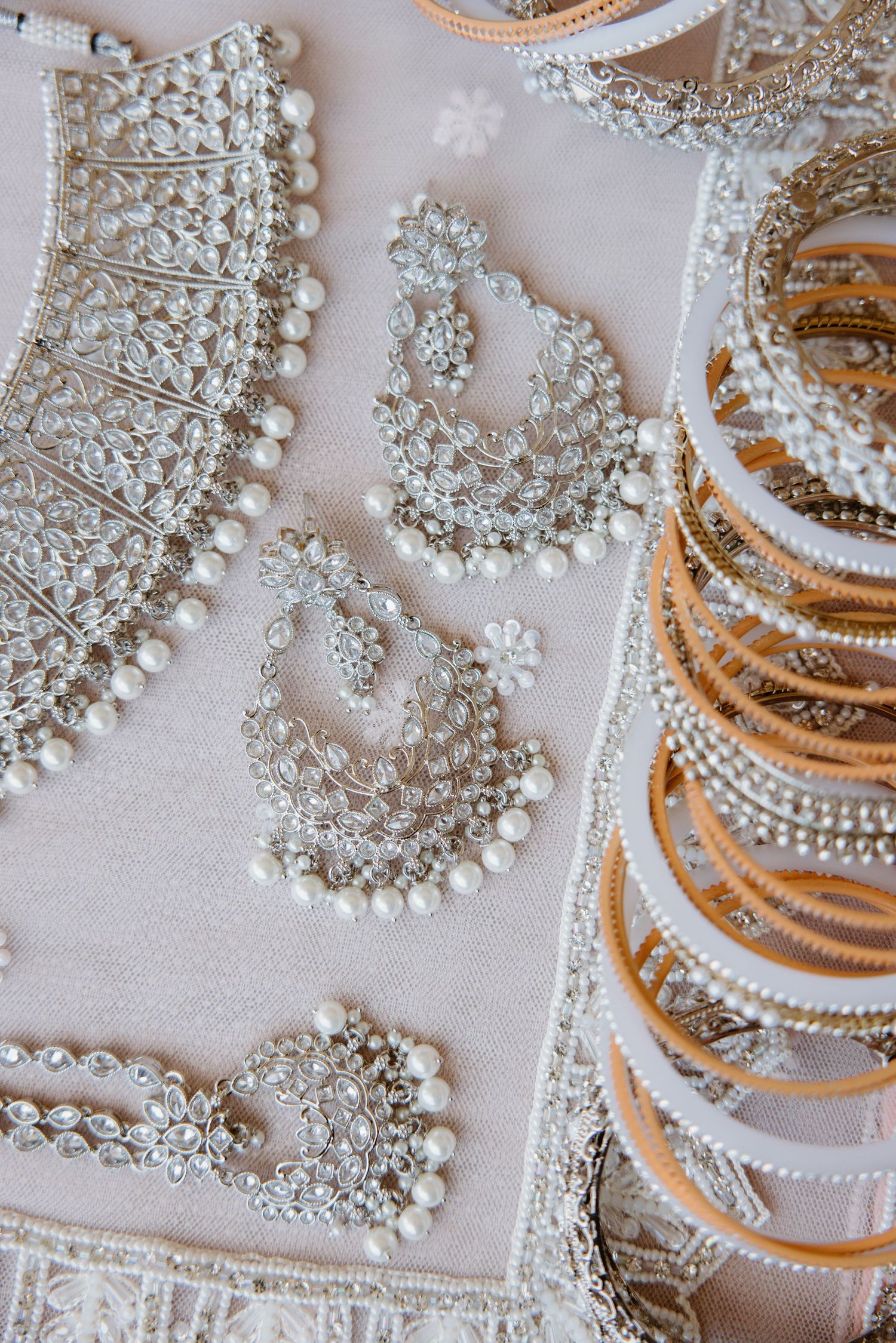 Elegant bridal jewelry collection featuring ornate pearl and crystal earrings and necklaces laid on light fabric.