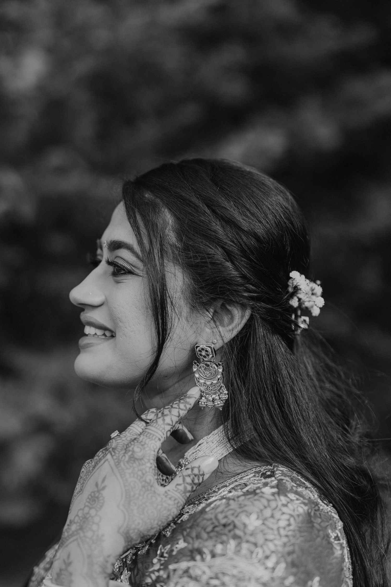 Black and white profile portrait of a person in traditional South Asian bridal attire with ornate jewelry and flowers in hair.