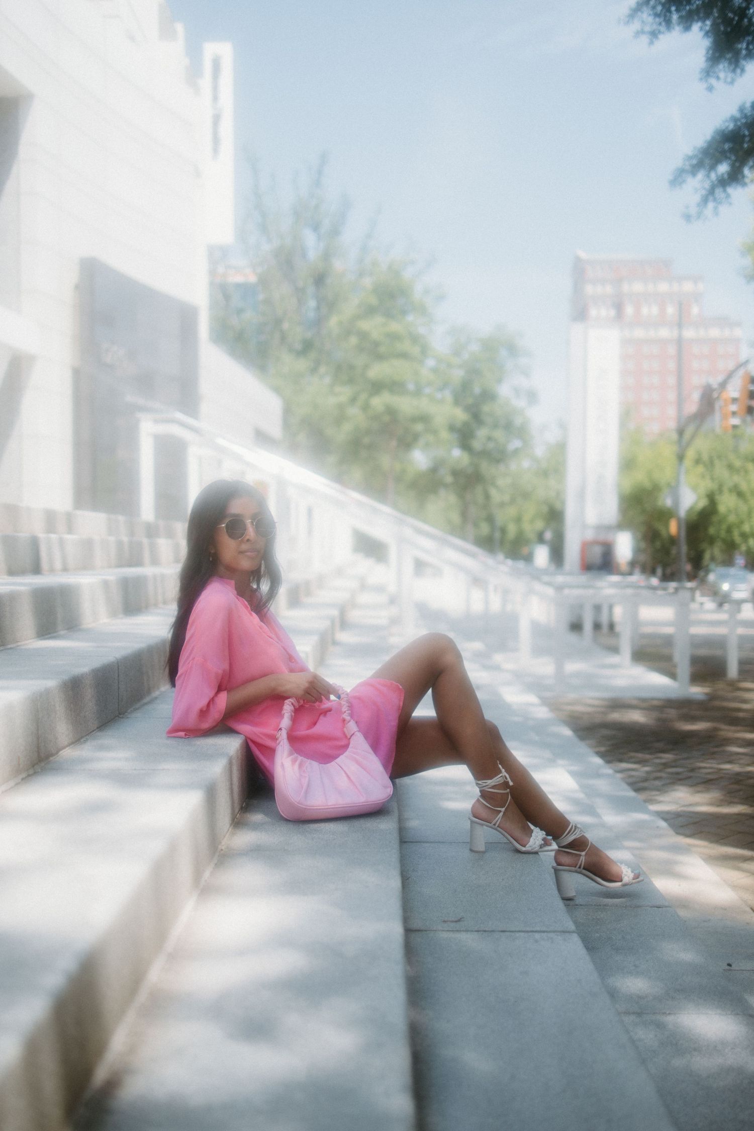 A dreamy summer scene with someone in a pink outfit relaxing on white concrete steps in soft sunlight.