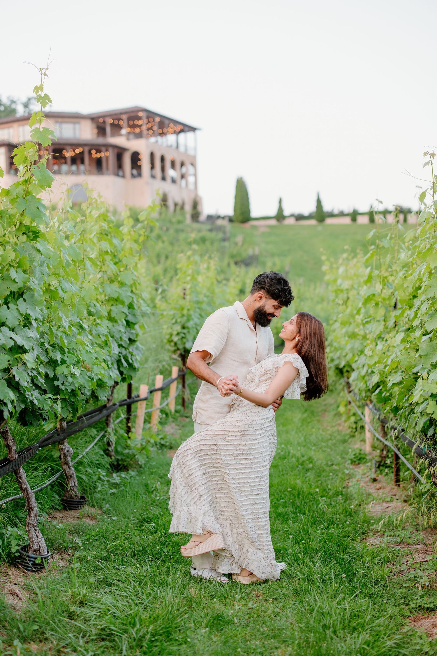 Two people share a romantic moment while sitting among vineyard rows on a sunny afternoon at a winery.