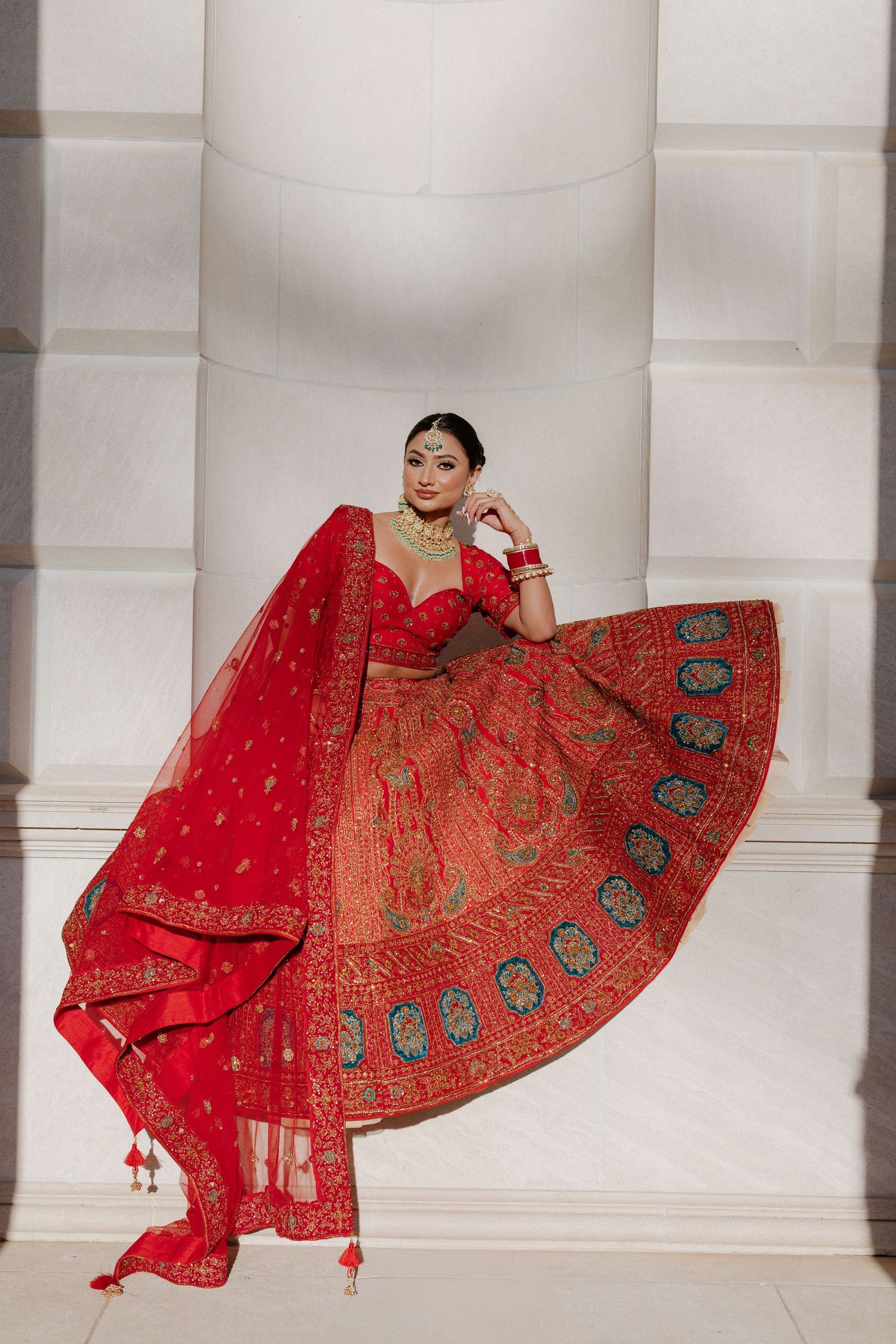 Elegant red and gold Indian lehenga with intricate embroidery twirls against white pillared backdrop.