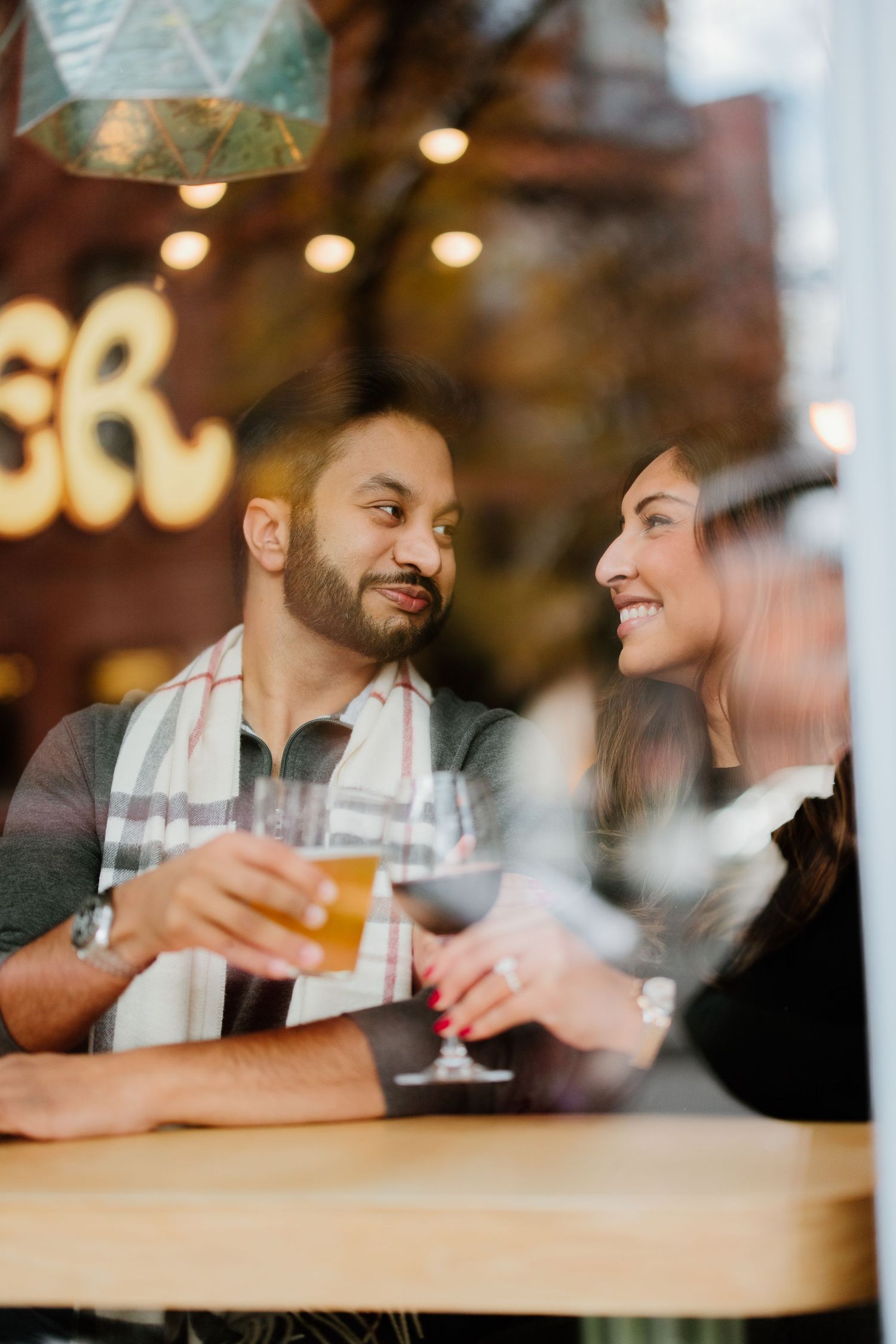 Two people having drinks and conversation at a bar counter with warm lighting and a cozy ambiance.