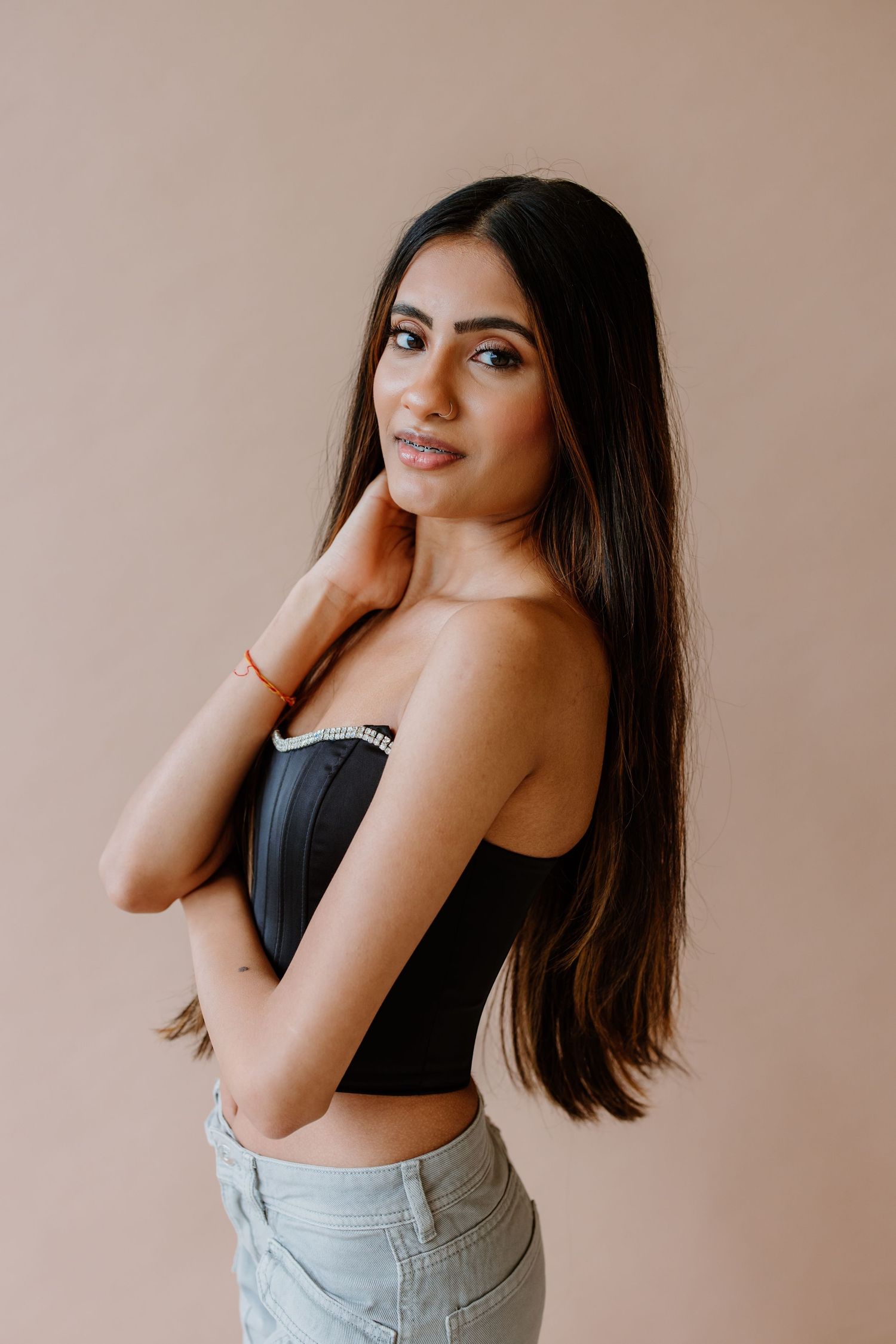 Portrait shot of someone posing in a black corset top and light denim jeans against a beige background.