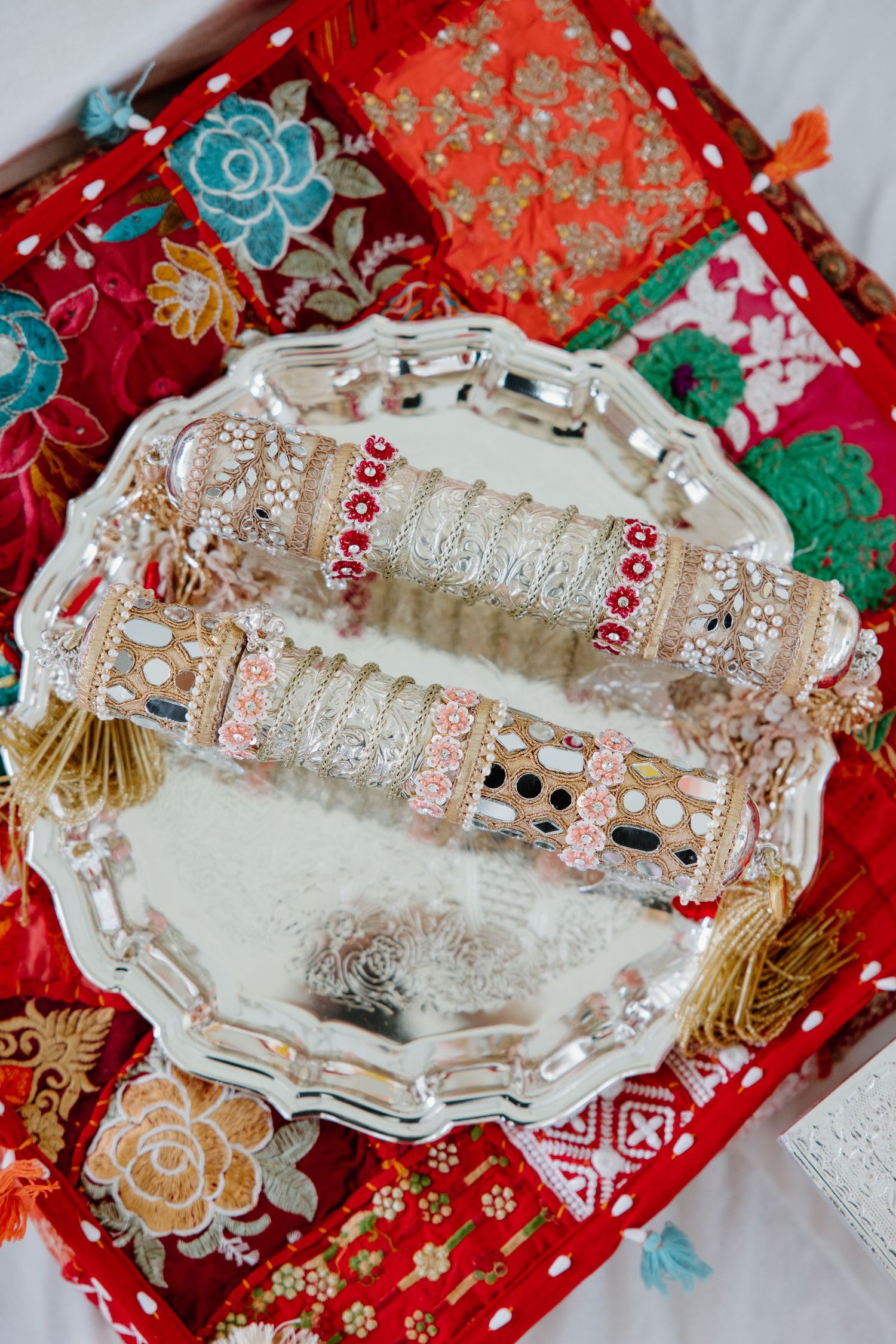 Decorative silver metal plates with intricate patterns displayed on festive red and gold floral patterned fabrics.