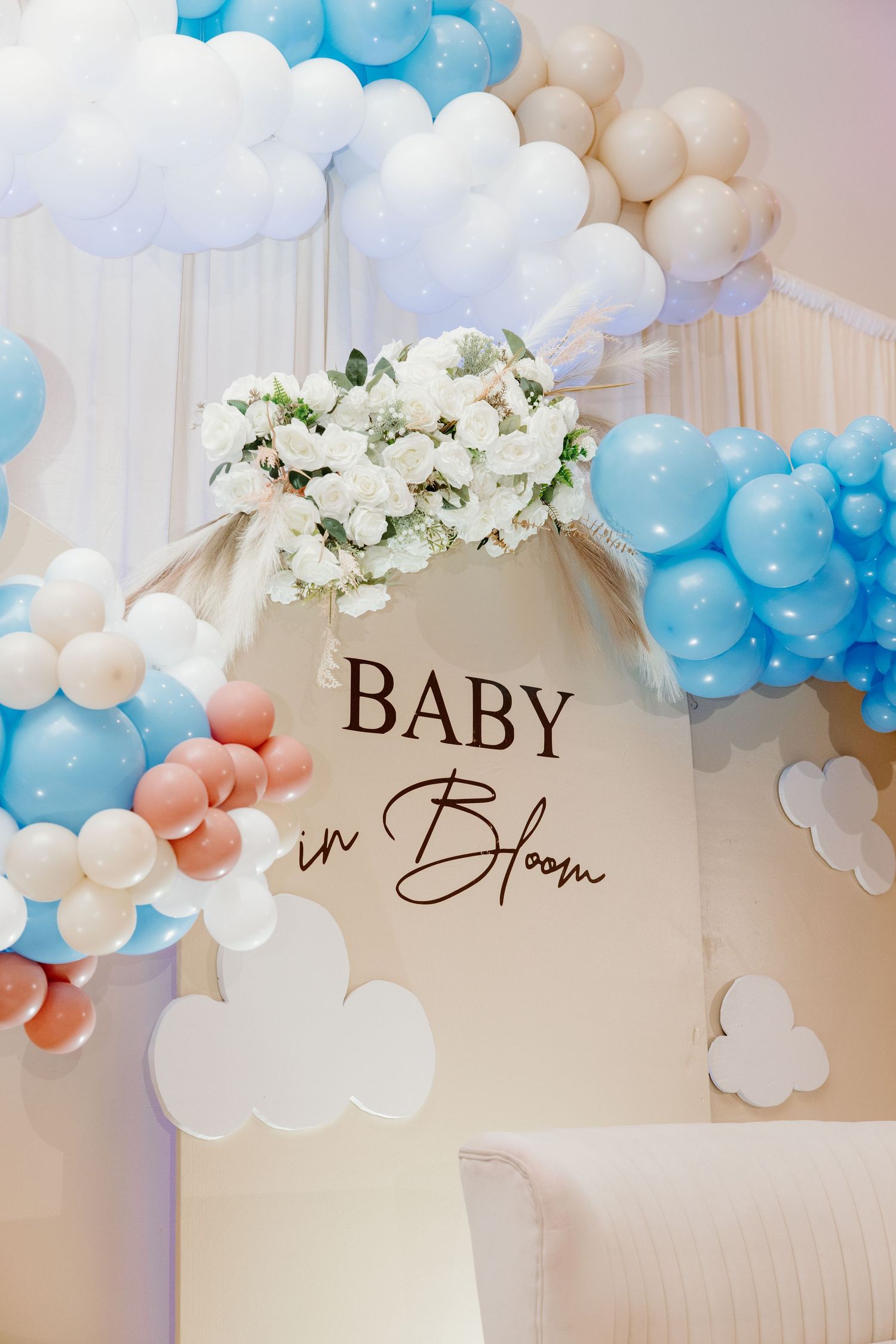 White and blue balloon arch decoration with floral accents and 'BABY' text for a stylish baby shower celebration.