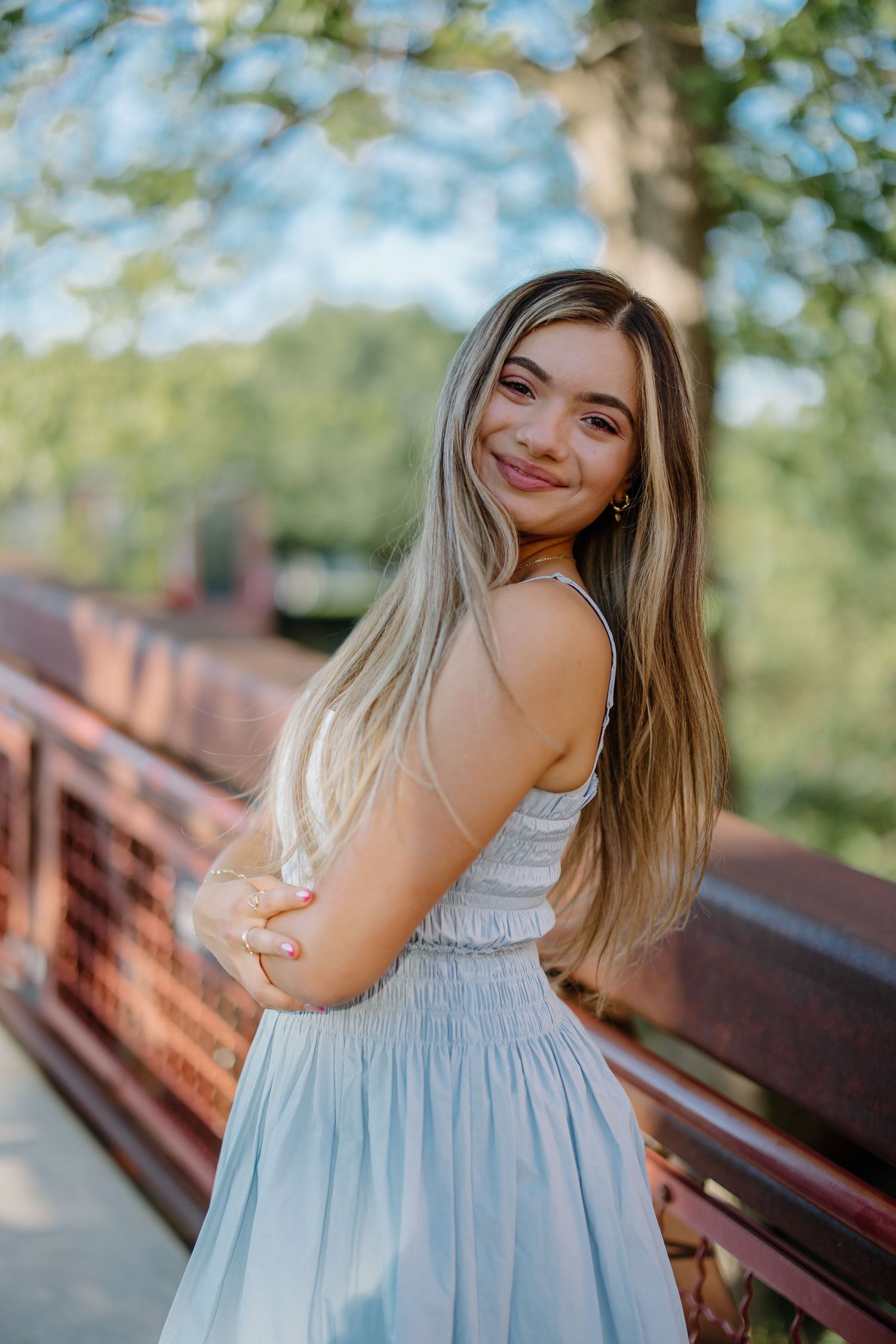 Portrait series in dreamy lighting shows person in light blue summer dress posing on wooden bridge.