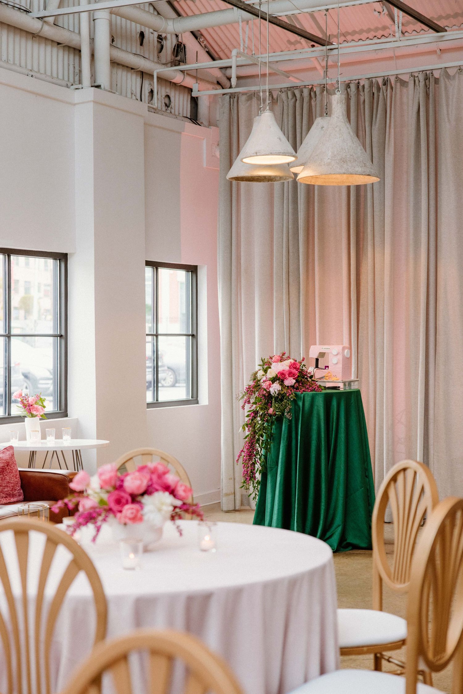 Elegant event space with romantic pink lighting, white tablecloths, and emerald green curtains decorating the modern venue.