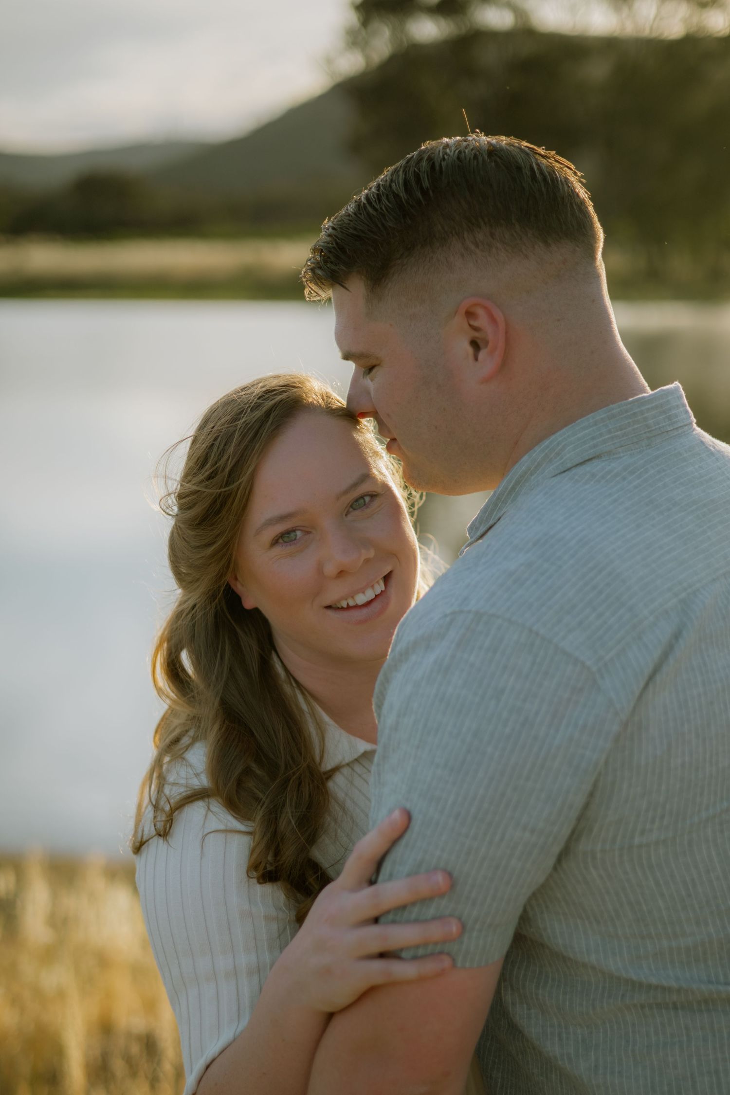 A romantic couple embraces in a field at sunset as golden light illuminates their tender moment together.