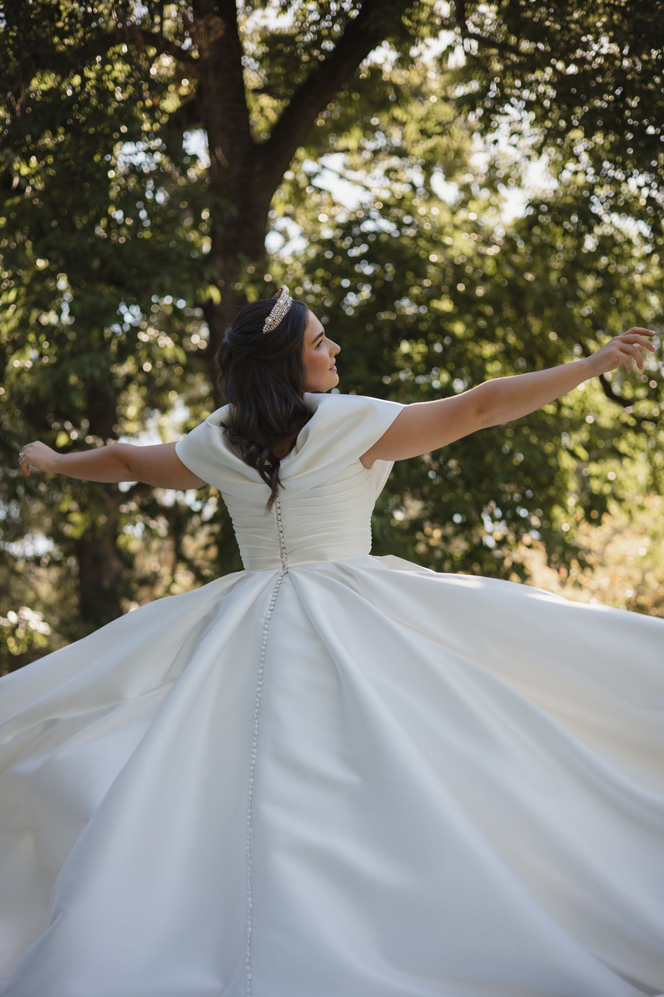 A person in a wedding dress spins gracefully in a sunlit garden setting, creating a twirling motion effect.