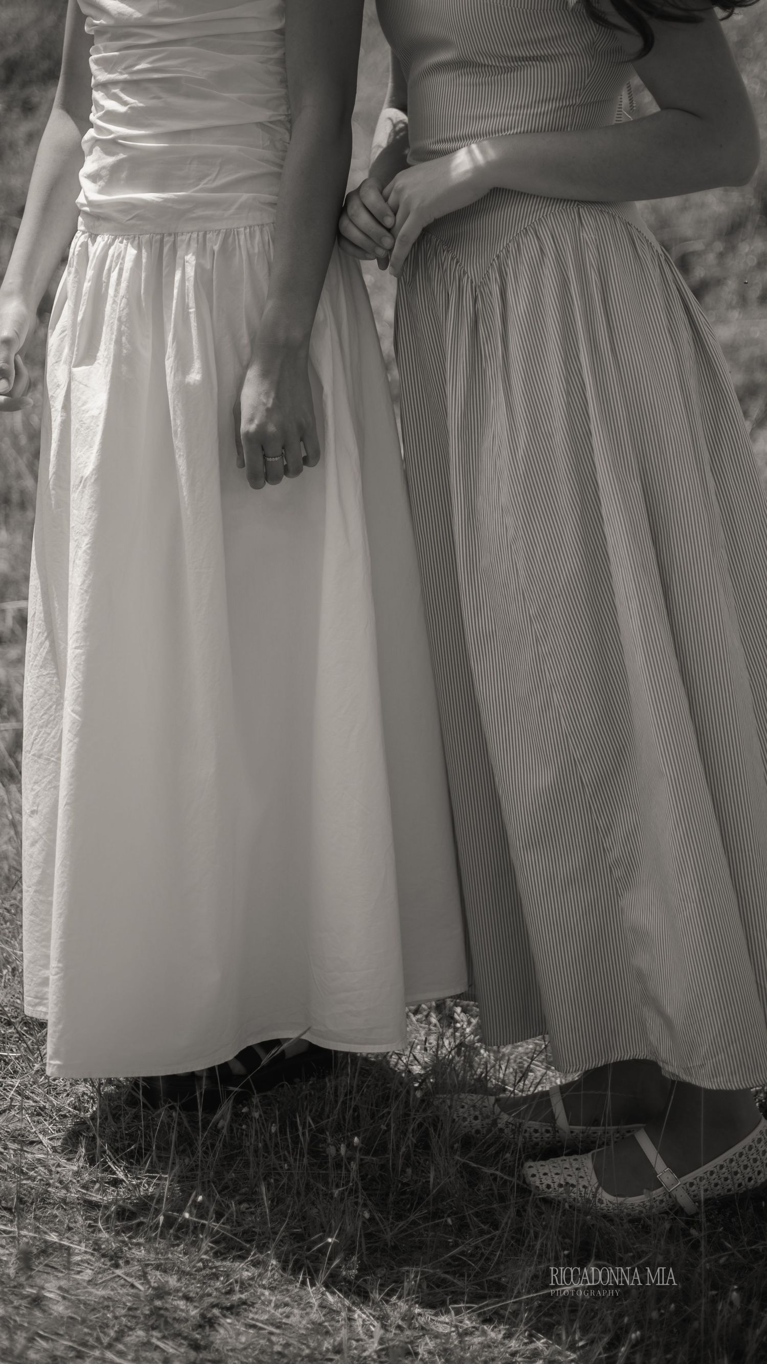 Black and white image showing the bottom portions of vintage white dresses against a dark grassy background.