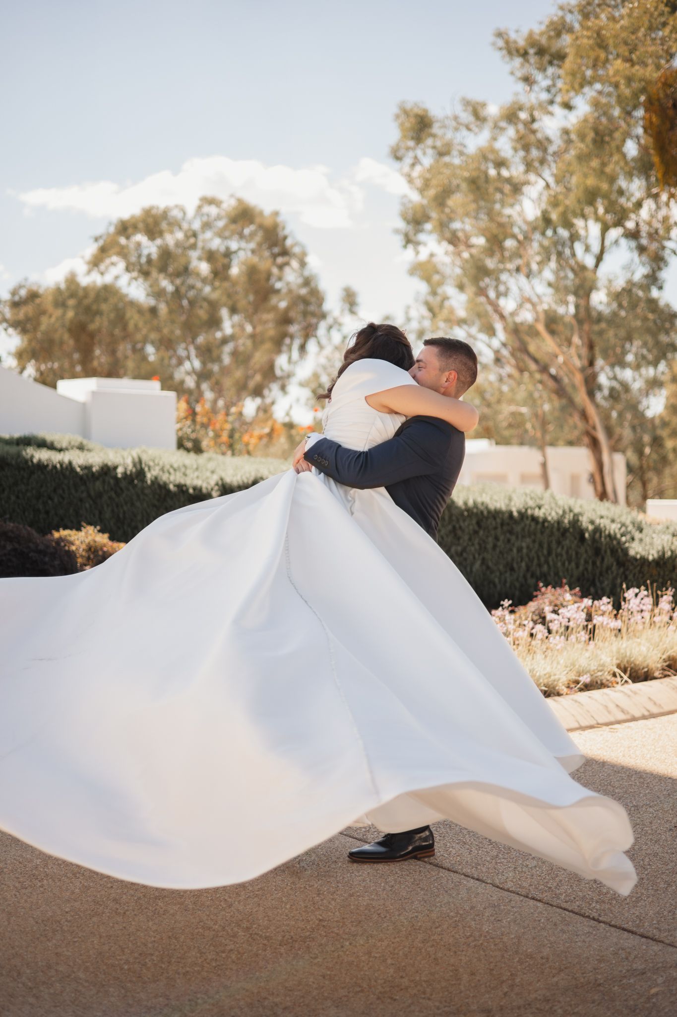 A romantic wedding moment captured in sunlight as a flowing white dress billows in the breeze against a natural backdrop.