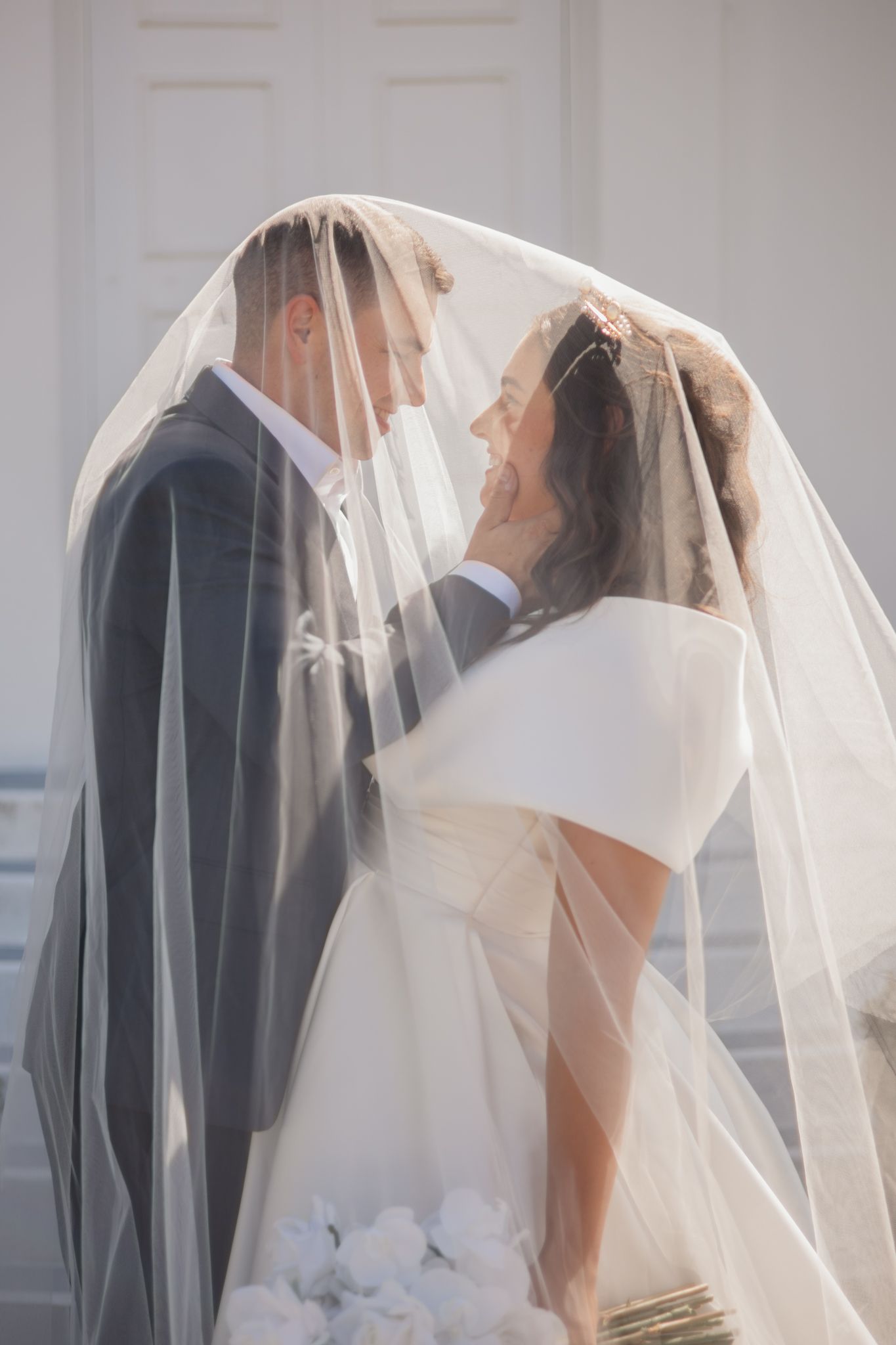Romantic bridal couple sharing an intimate moment under a flowing white veil during their wedding day.