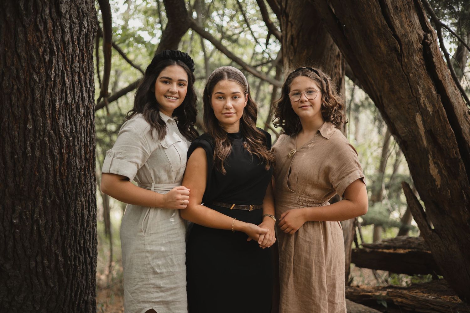 Three people in casual clothing pose together in an outdoor setting with trees in the background.