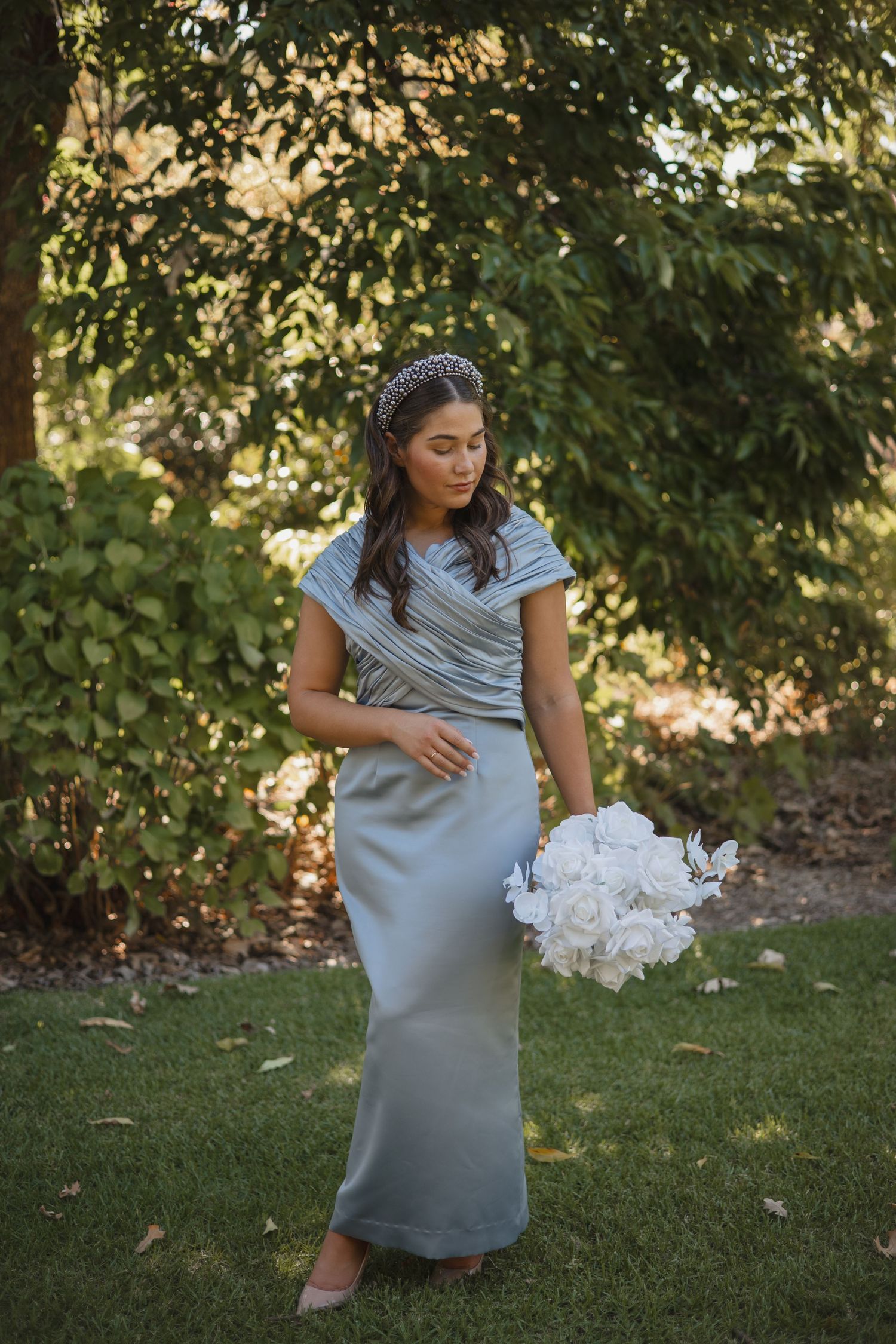 Someone in a soft blue striped dress holds a white bouquet while standing on grass in a garden setting.