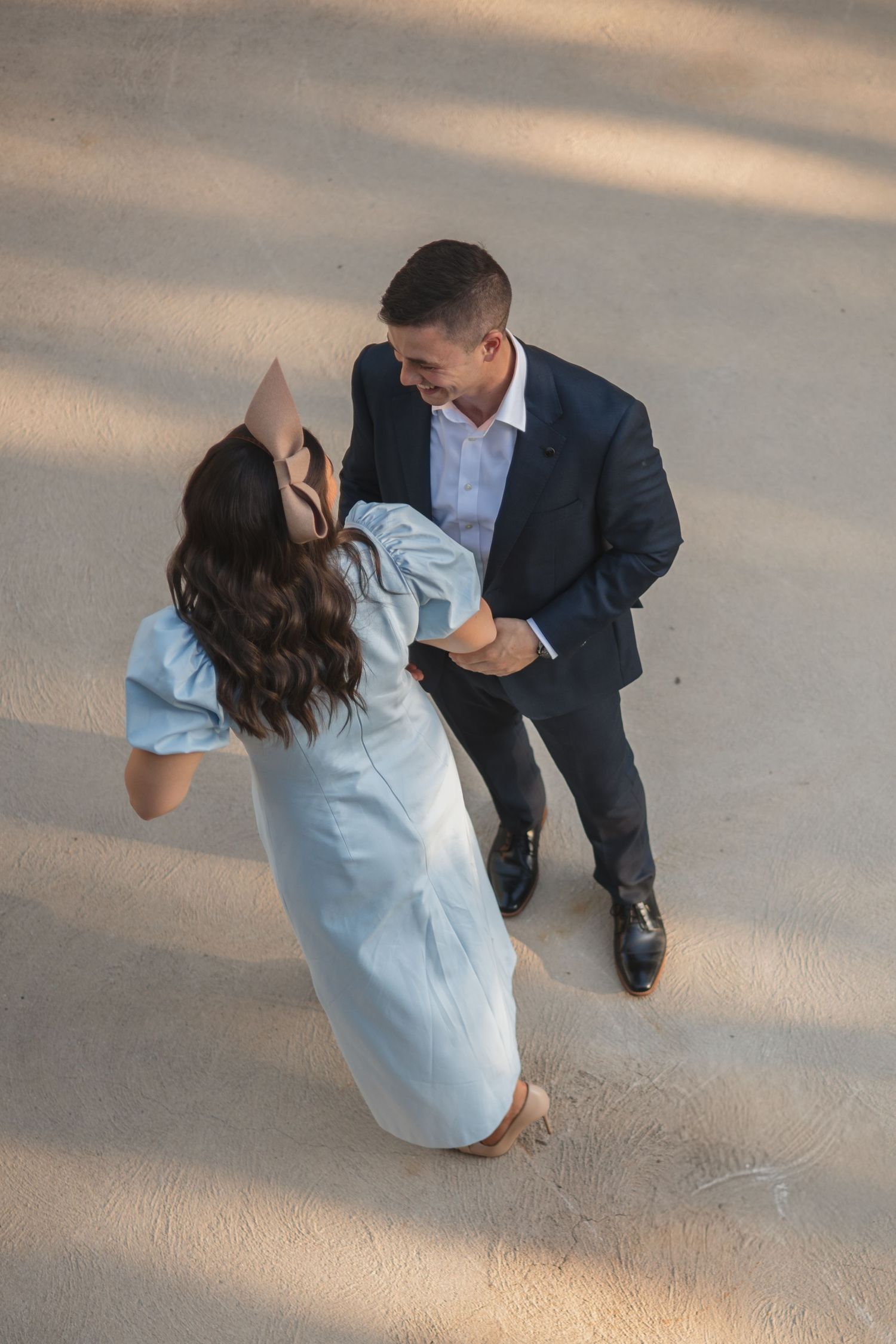 A couple dancing together on a beige floor, with the woman in a light blue dress and man in a navy suit.