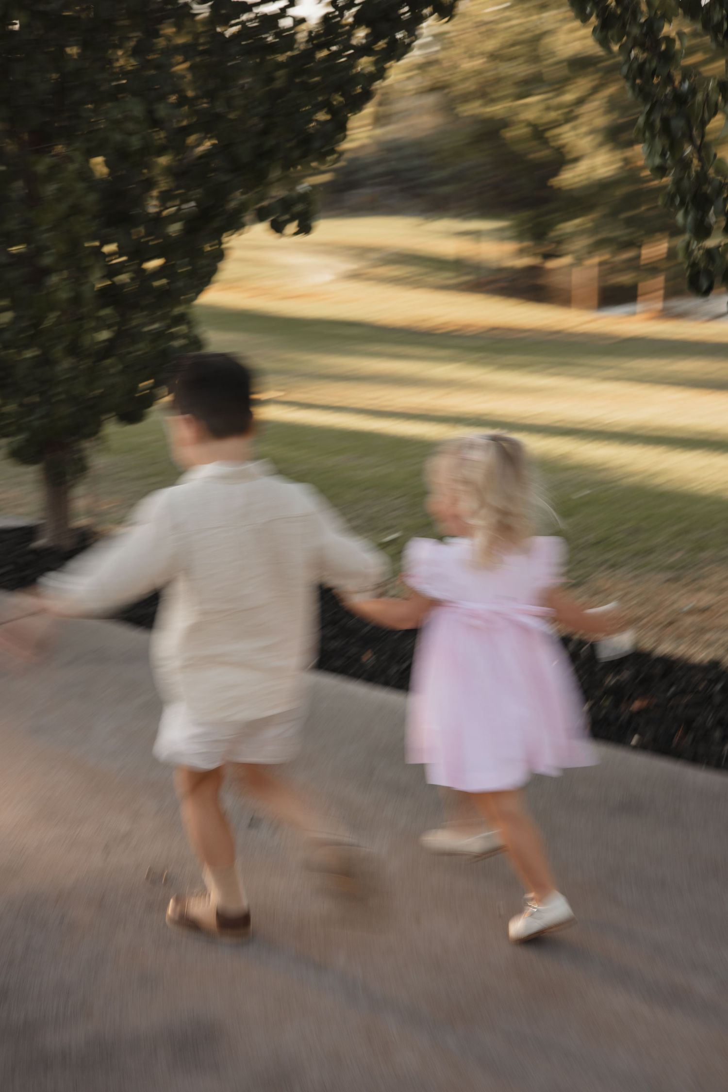 Blurred motion photo of two children running and holding hands on a path at sunset in summer.