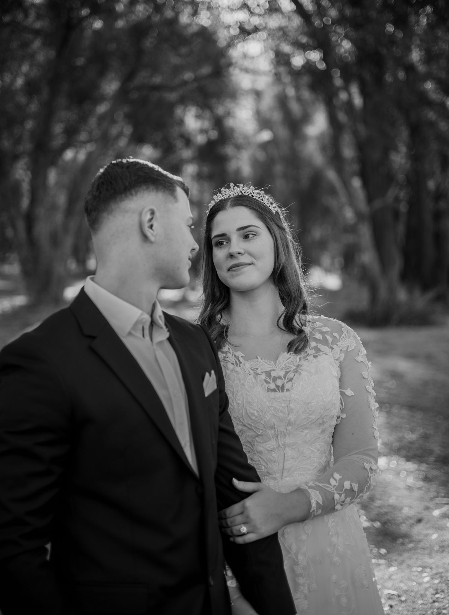 Black and white wedding photo series showing a couple in formal attire sharing intimate moments in a forest setting.