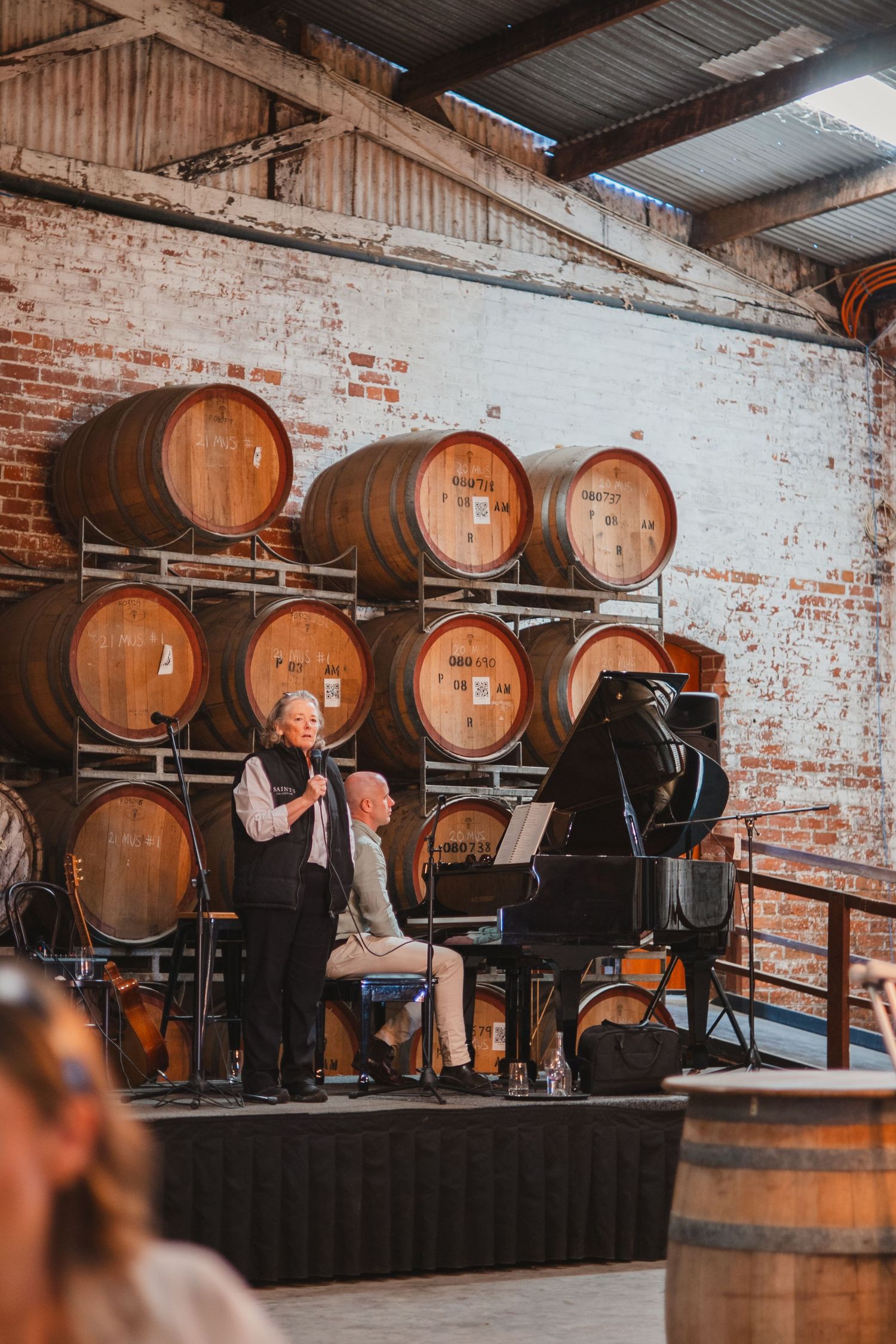 Musicians perform classical music on a stage with wooden wine barrels stacked against a rustic brick wall backdrop.