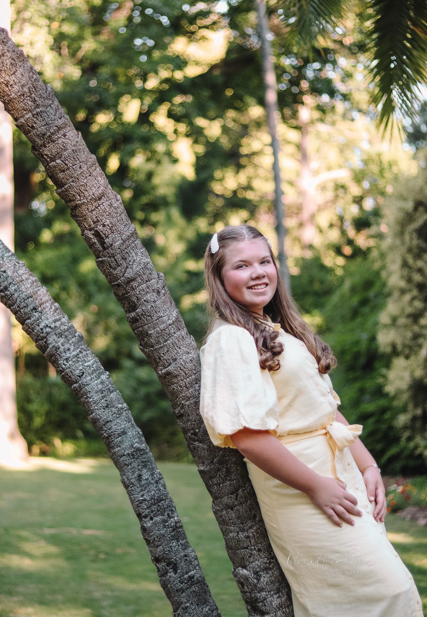 Three photos of someone in a yellow dress posing casually against a tree trunk in a sunlit outdoor garden setting.