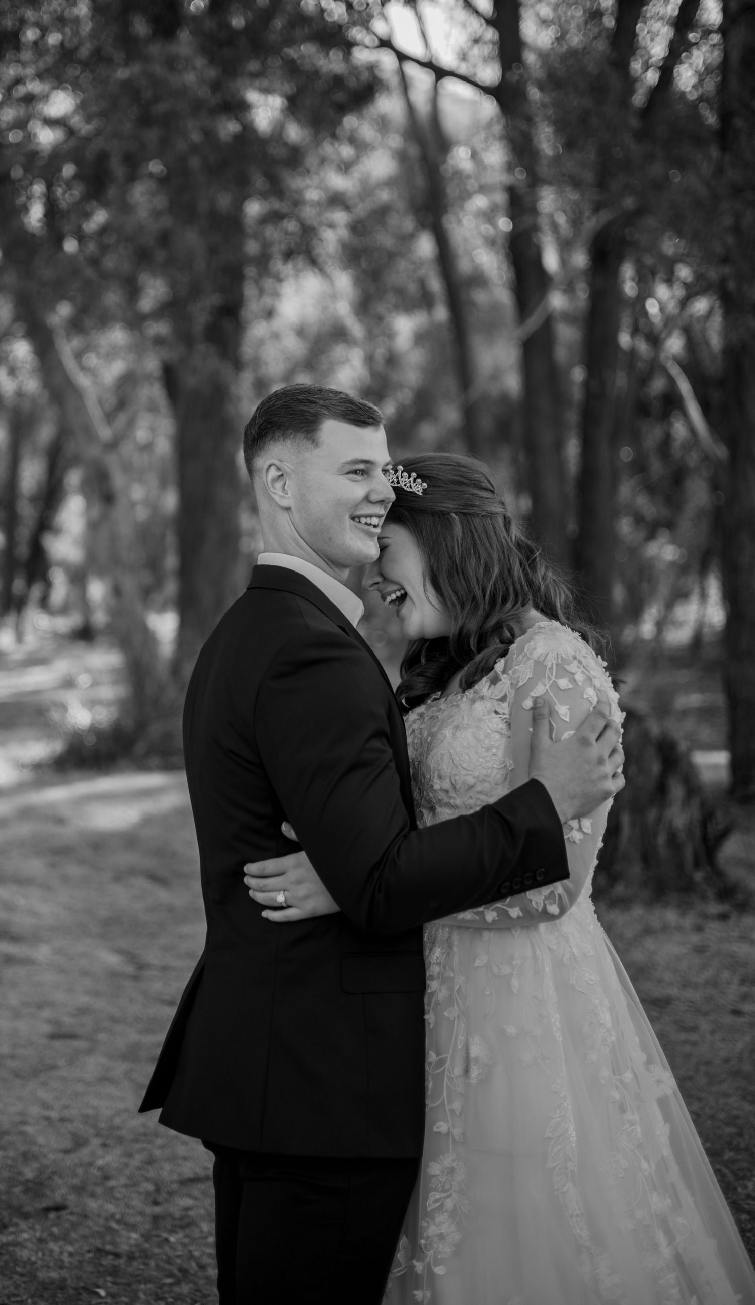 A romantic black and white wedding photoshoot in a wooded setting shows a couple sharing joyful candid moments together.
