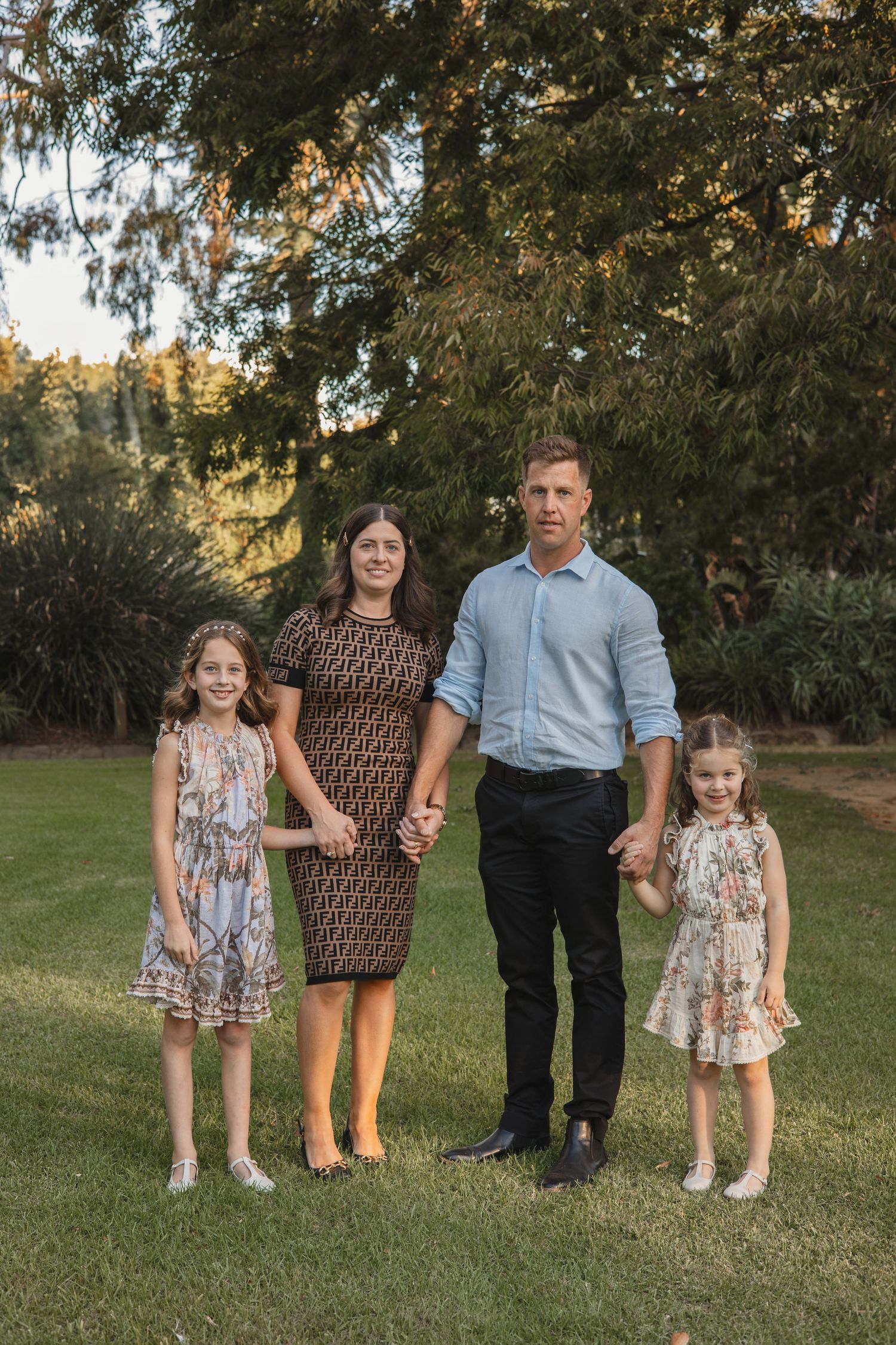 A family poses together on a grassy lawn during a sunny outdoor photo session.