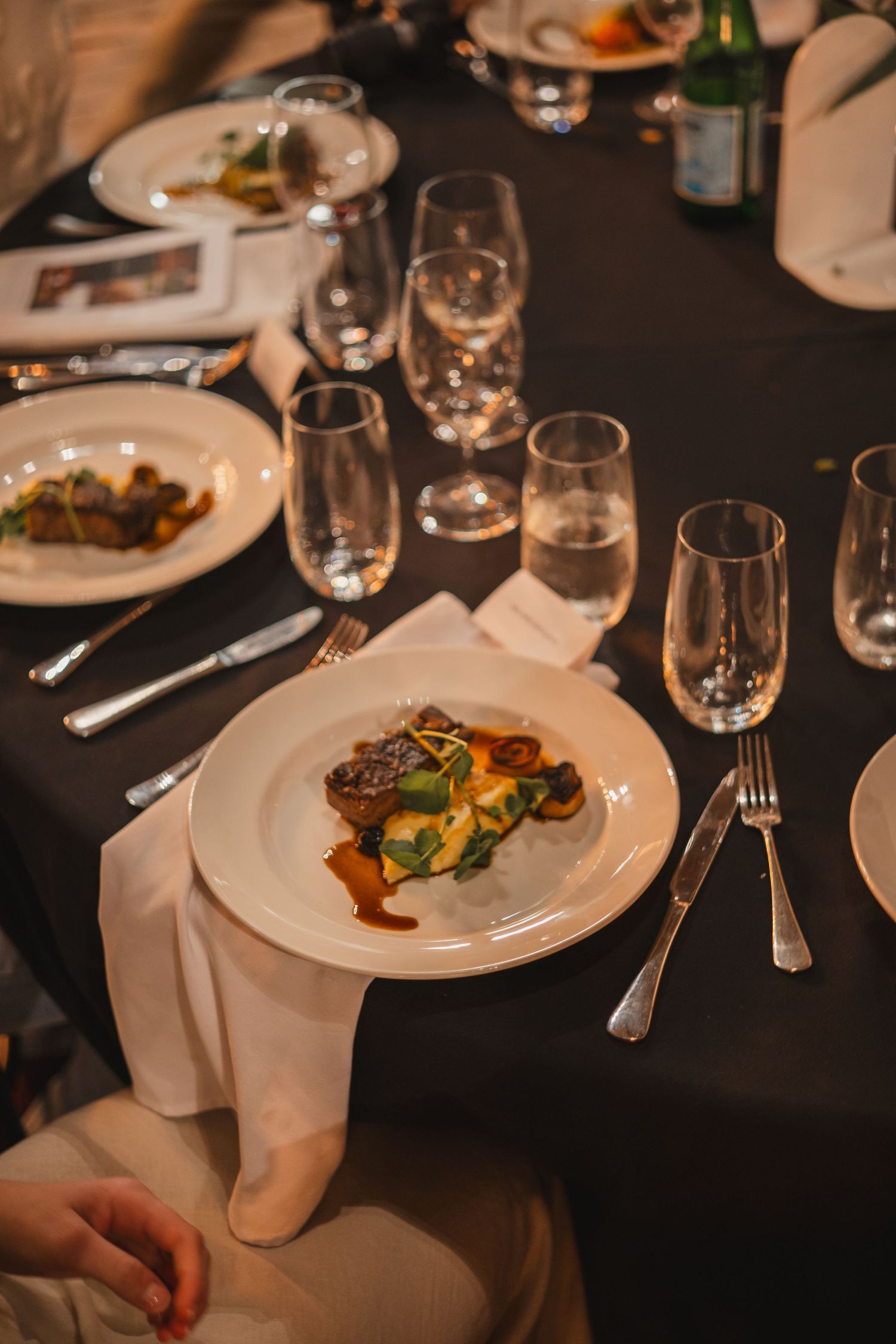 An elegant dinner table setting with plated dishes and wine glasses in a dimly lit fine dining restaurant.