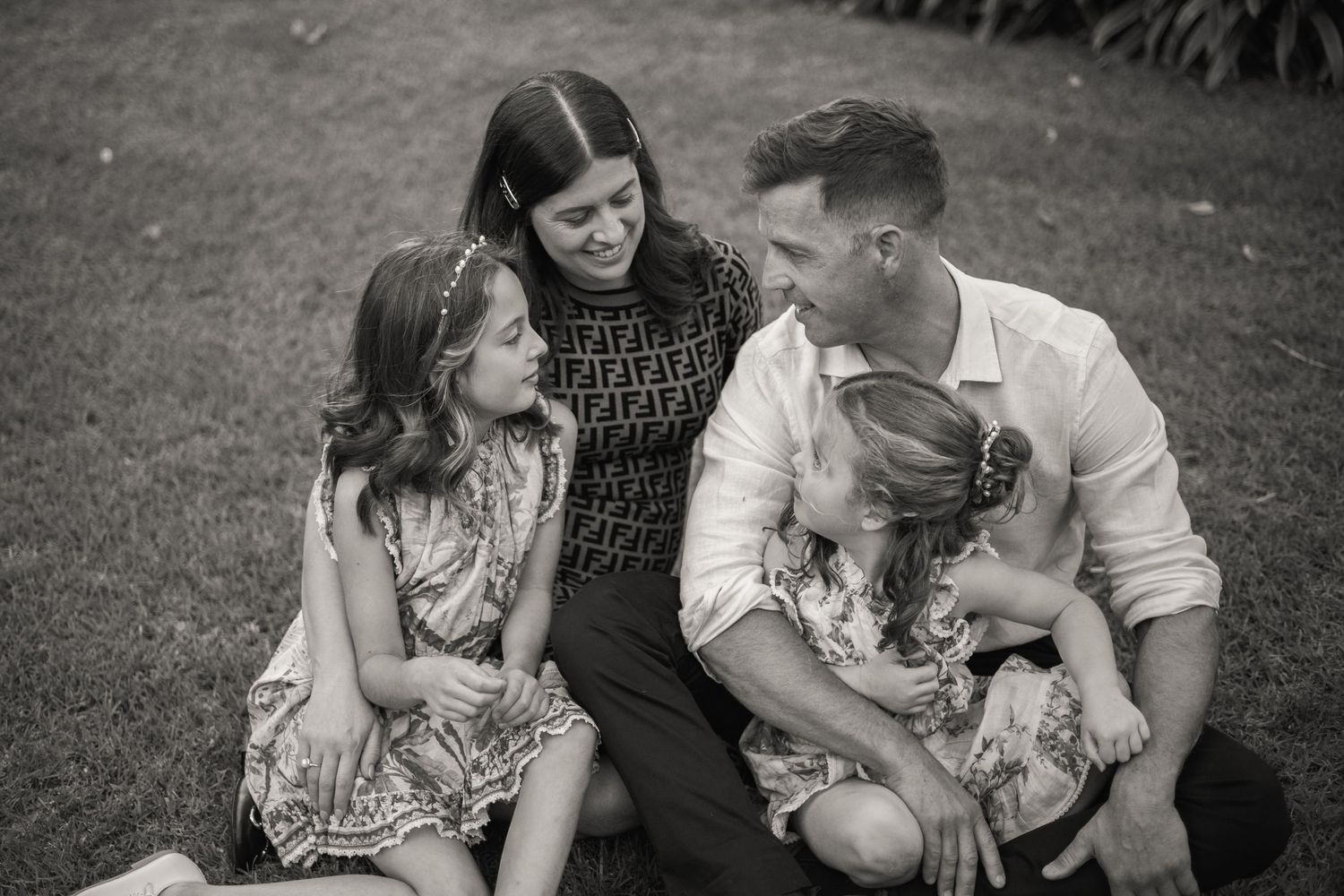 A loving family sits together on grass sharing a tender moment in black and white photography.