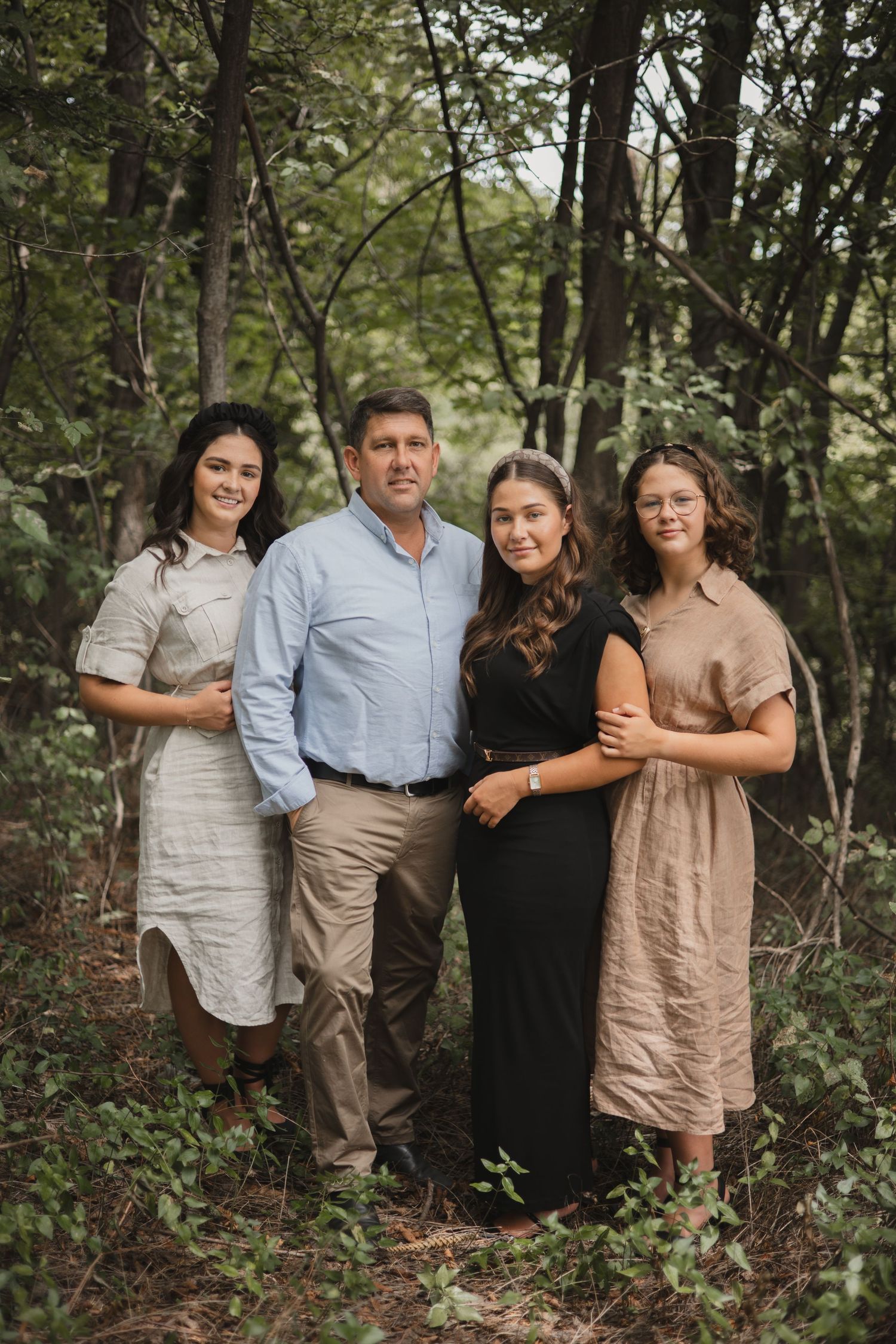 A family poses together for outdoor portraits in a wooded natural setting wearing coordinated neutral-toned clothing.