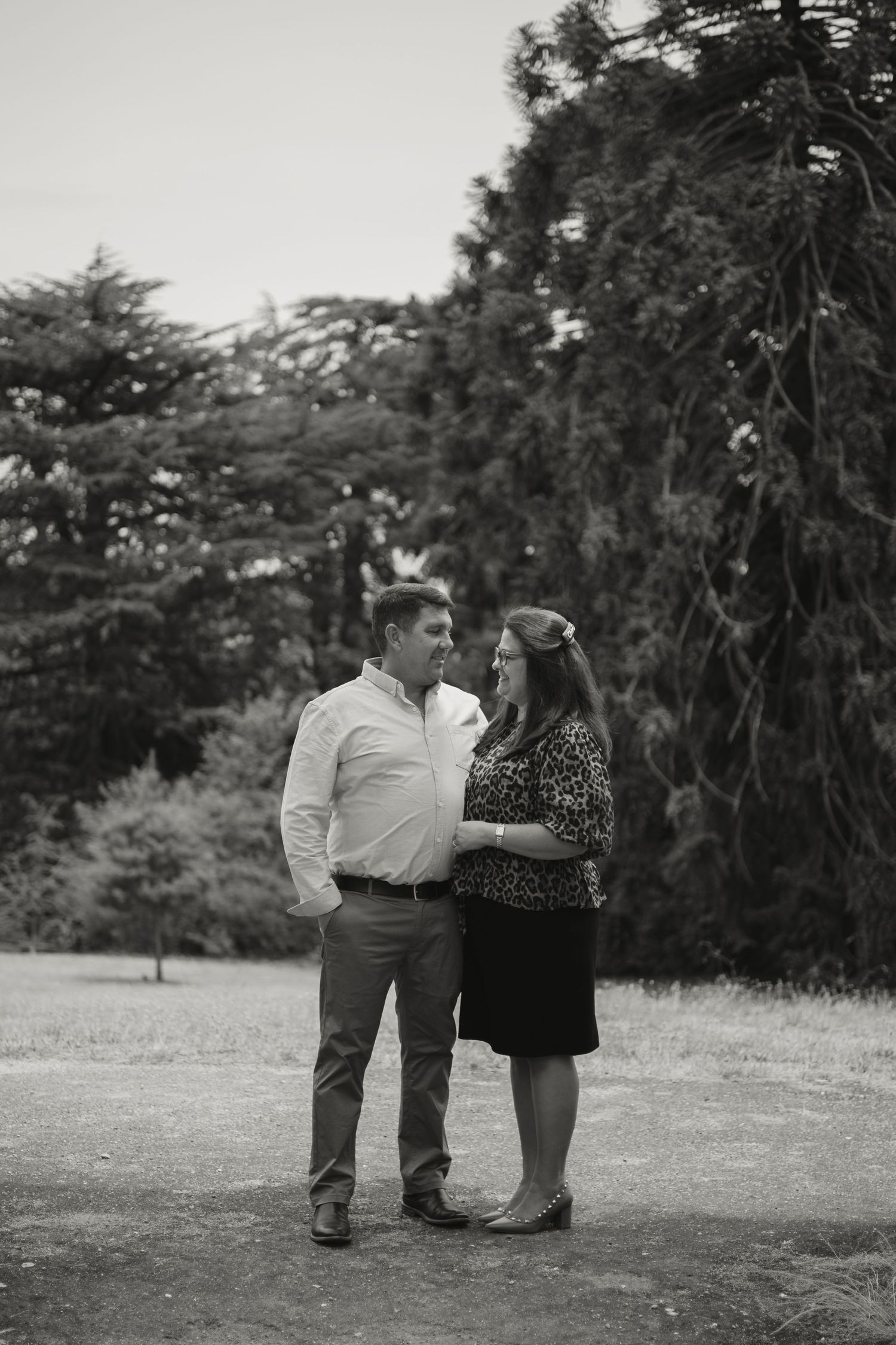 A romantic couple shares an intimate outdoor moment in nature captured in black and white photography.