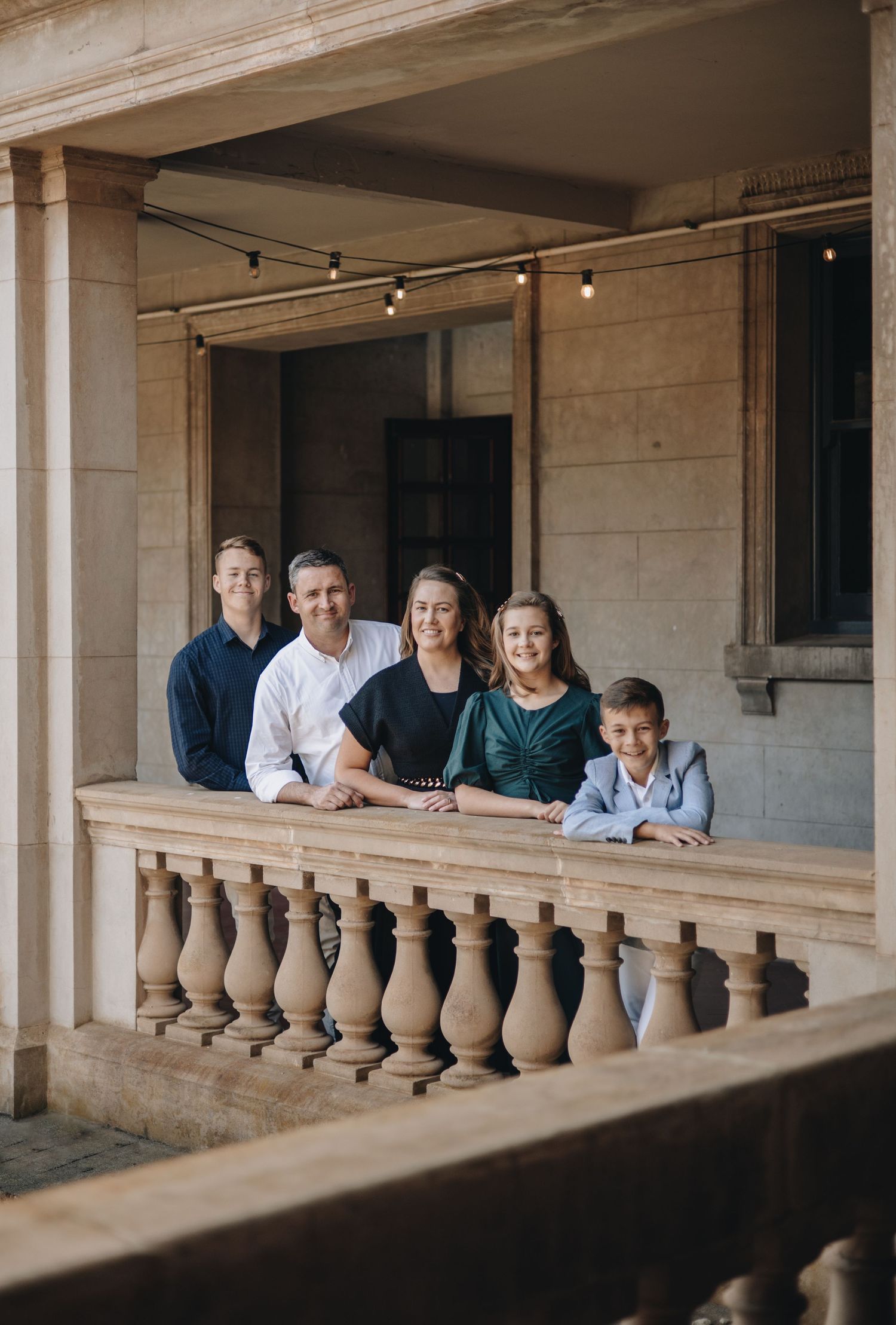 A group stands together on a historic stone balcony with decorative balusters and warm overhead lighting.