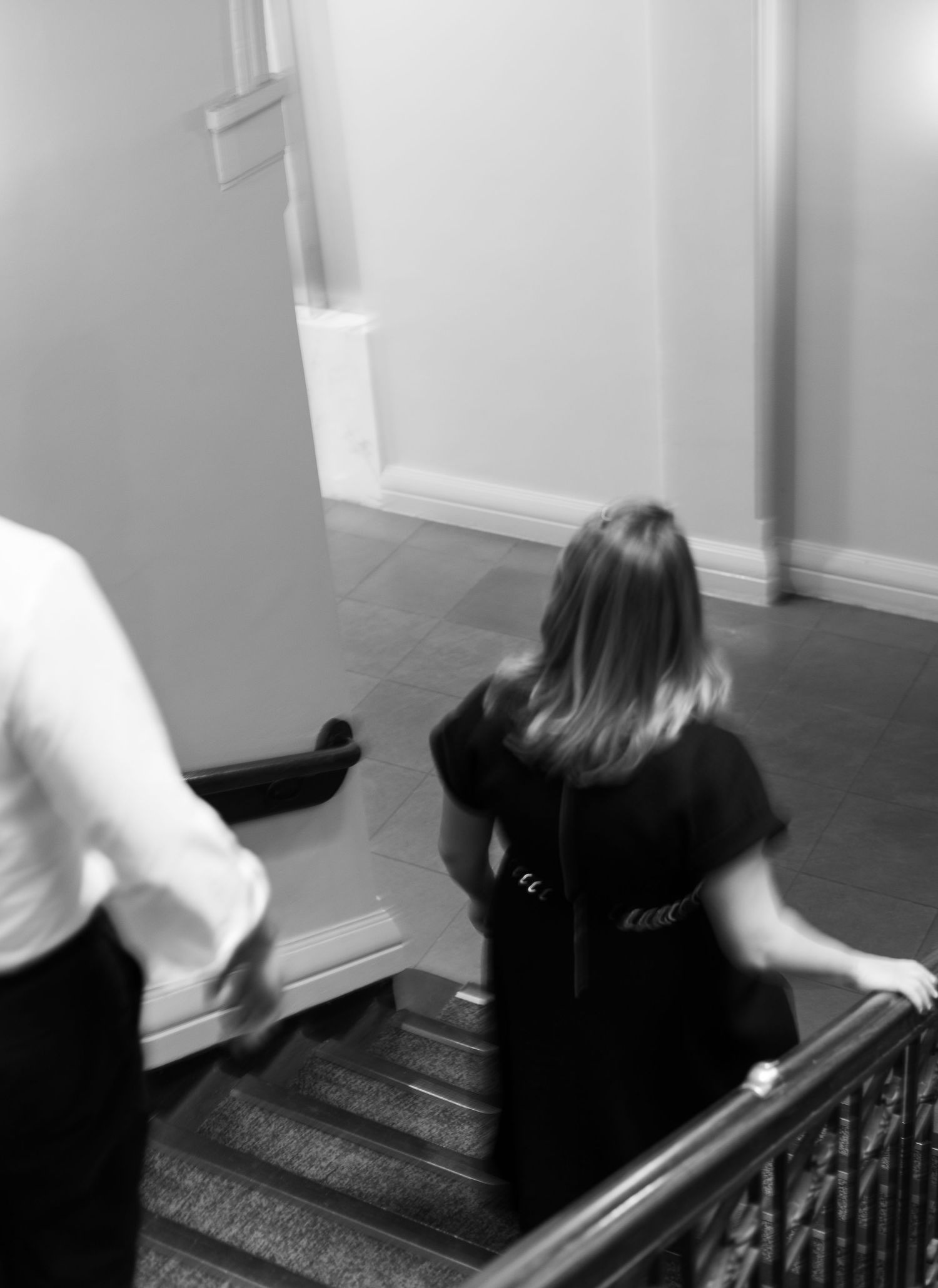 People descending a dark staircase in black and white with motion blur effect and railing visible.