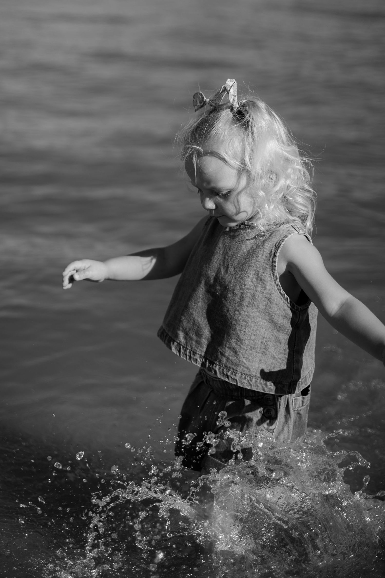 A young child in a sleeveless top splashes joyfully in water, captured in black and white photography.