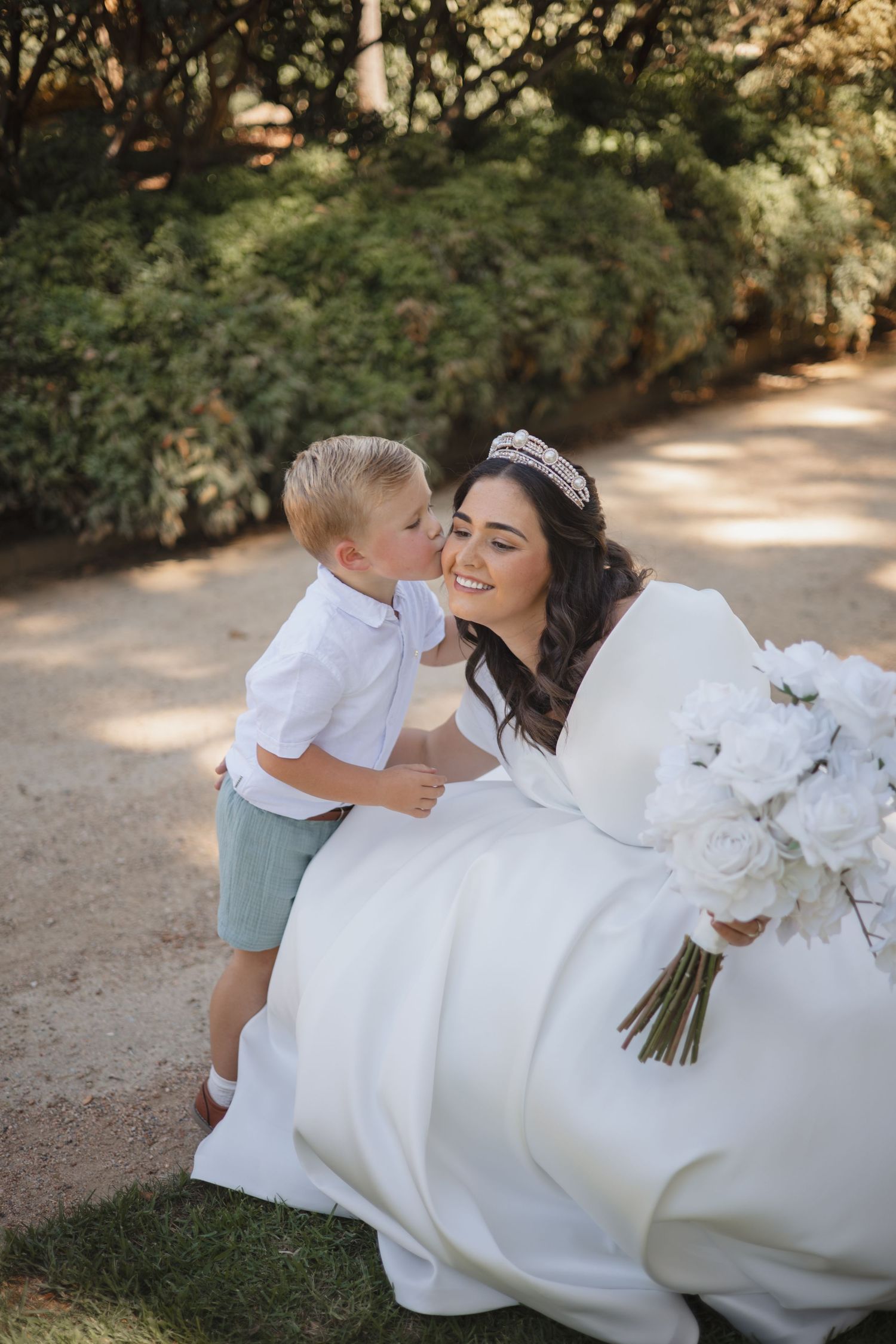 A sweet moment shared at a wedding as a young boy in white shirt and mint shorts shows affection to a bride holding white flowers.