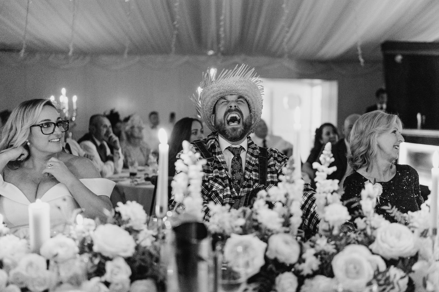 Black and white photo of wedding reception guests surrounded by elegant floral centerpieces.  Virginia Park Lodge Wedding Photographer Cavan