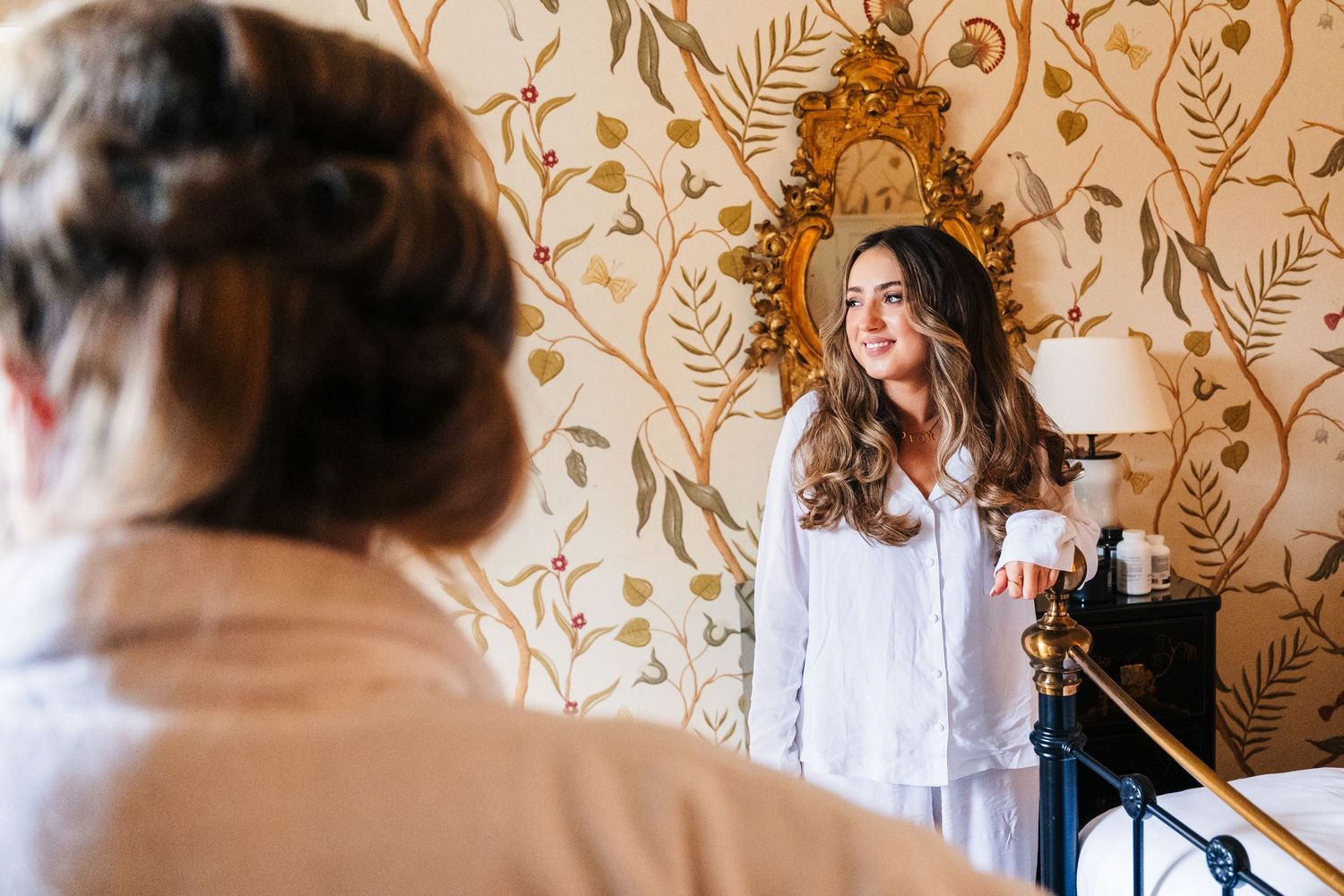 A person in white standing by a wall with elegant gold leaf pattern wallpaper during wedding preparations. Virginia Park Lodge Wedding Photo