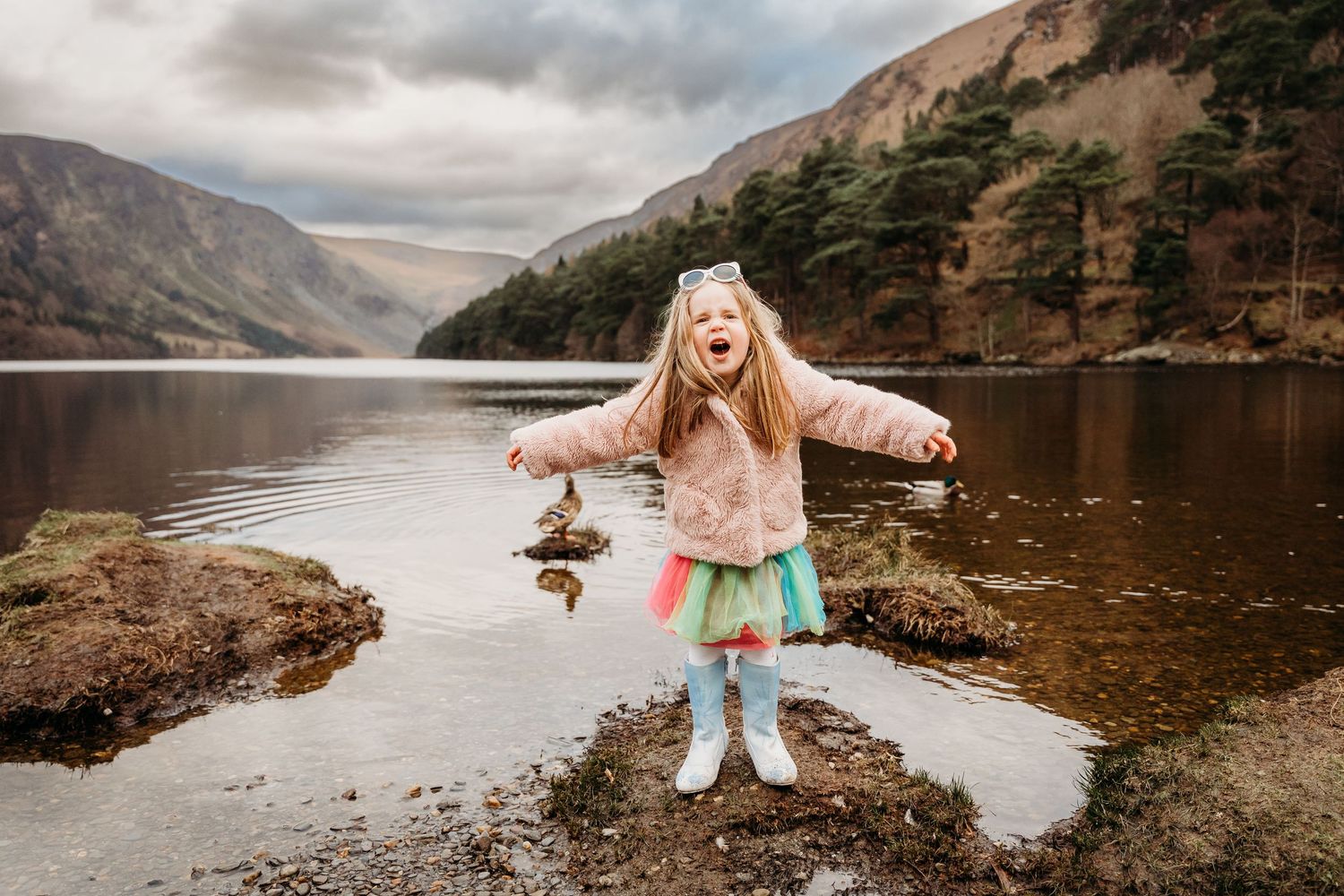 In a dramatic mountain landscape with a serene lake, someone dances joyfully along the rocky shoreline. family PHOTOGRAPHER Dublin