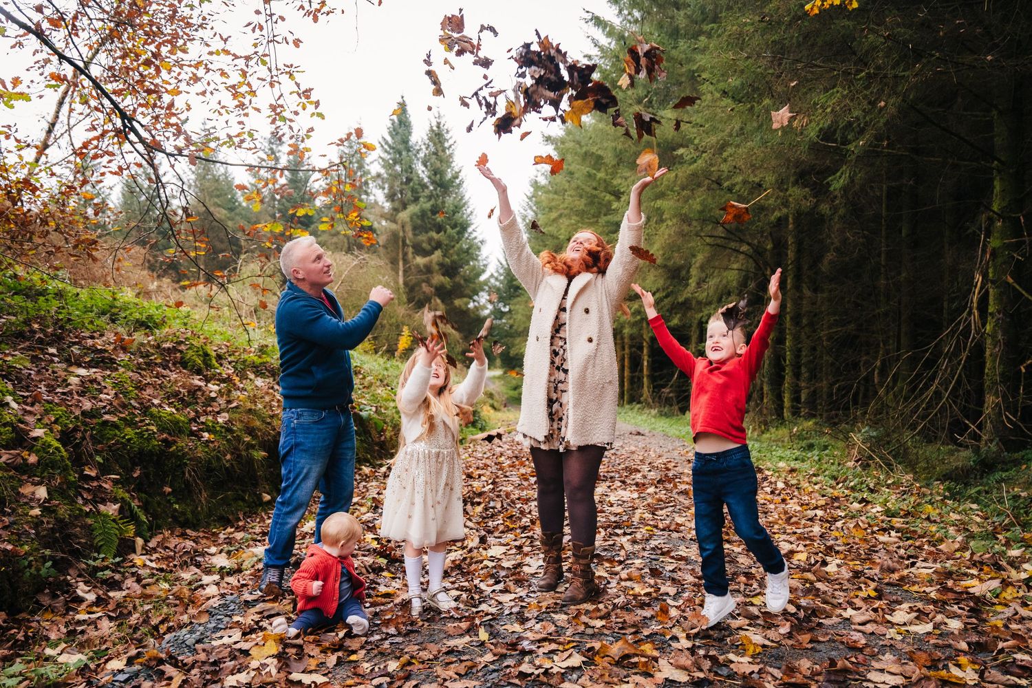People enjoying a playful fall photoshoot throwing colorful autumn leaves in the air at a wooded park location. family PHOTOGRAPHER Dublin