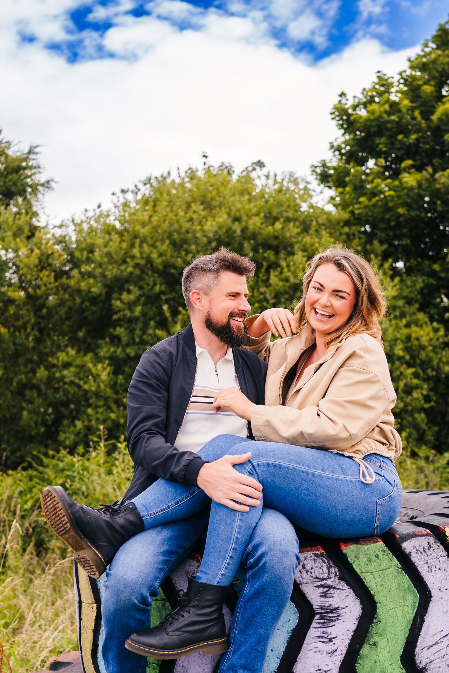 Couple sits together outdoors sharing a loving and playful moment on a sunny day with blue skies and green trees. PHOTOGRAPHER Dublin irelan