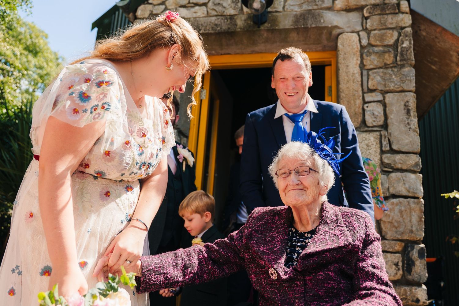 A sunny outdoor gathering shows people interacting near a stone building entrance. . Village Barn Tyrrellspass wedding photographer Ireland