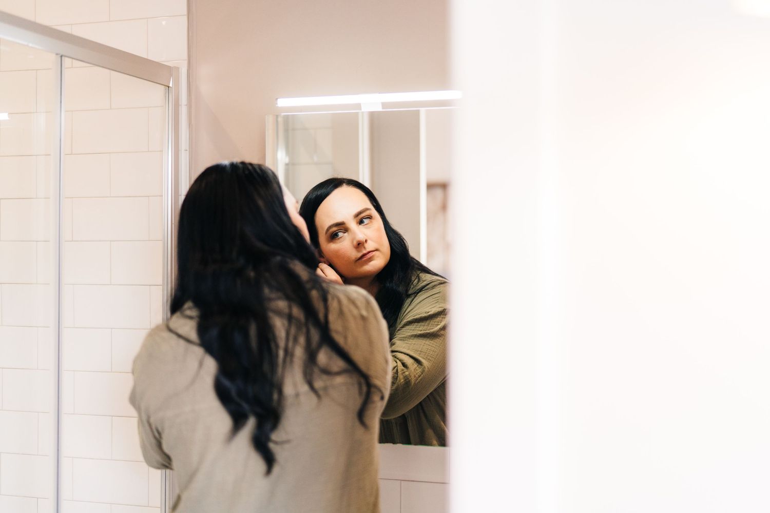 Person in a beige sweater looking thoughtfully at their reflection in a bathroom mirror. House Dublin Wedding Photographer