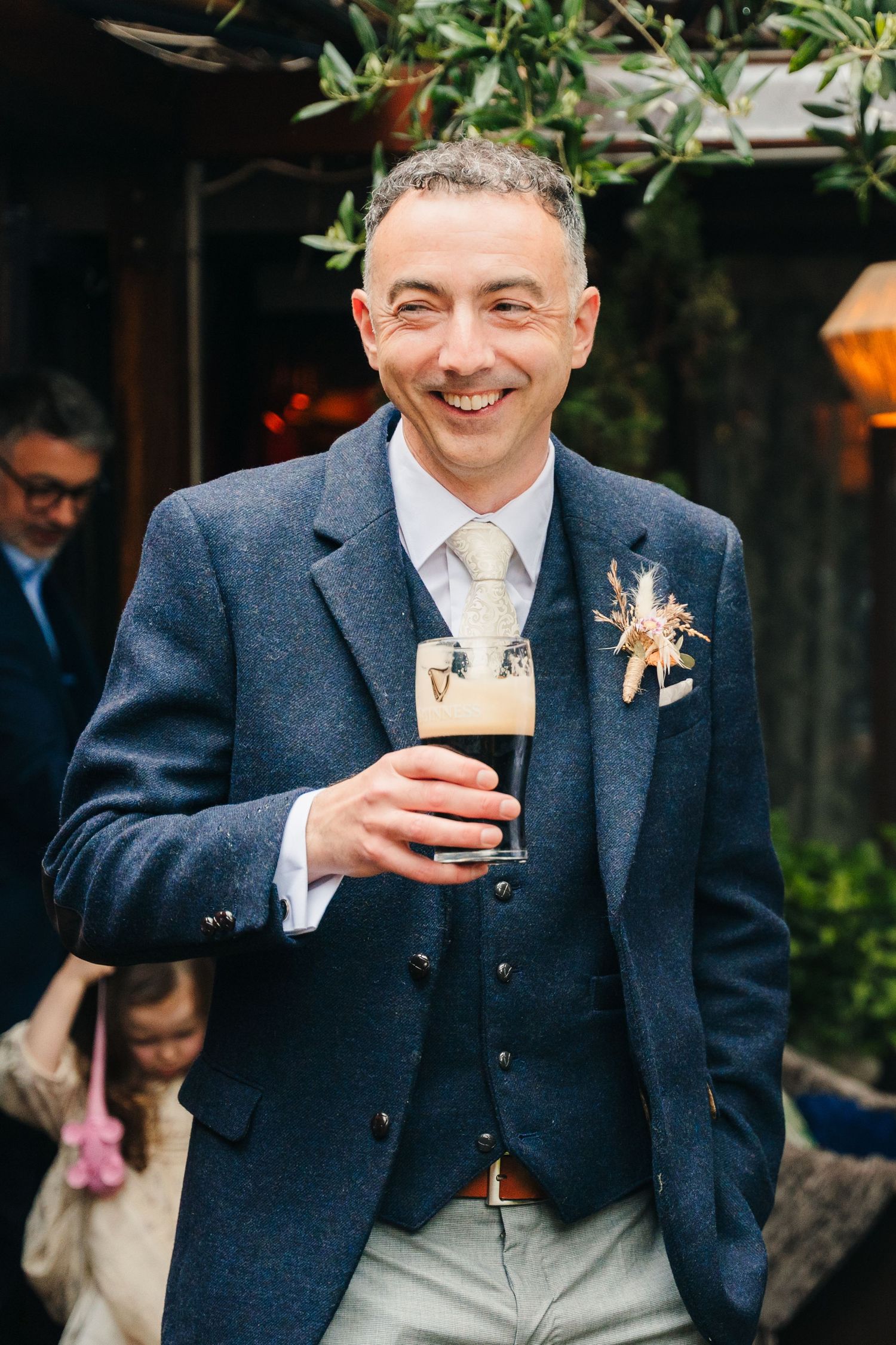 Wedding guest in navy suit enjoying a festive drink at an outdoor garden reception. Marco Pierre Dublin Wedding Photographer