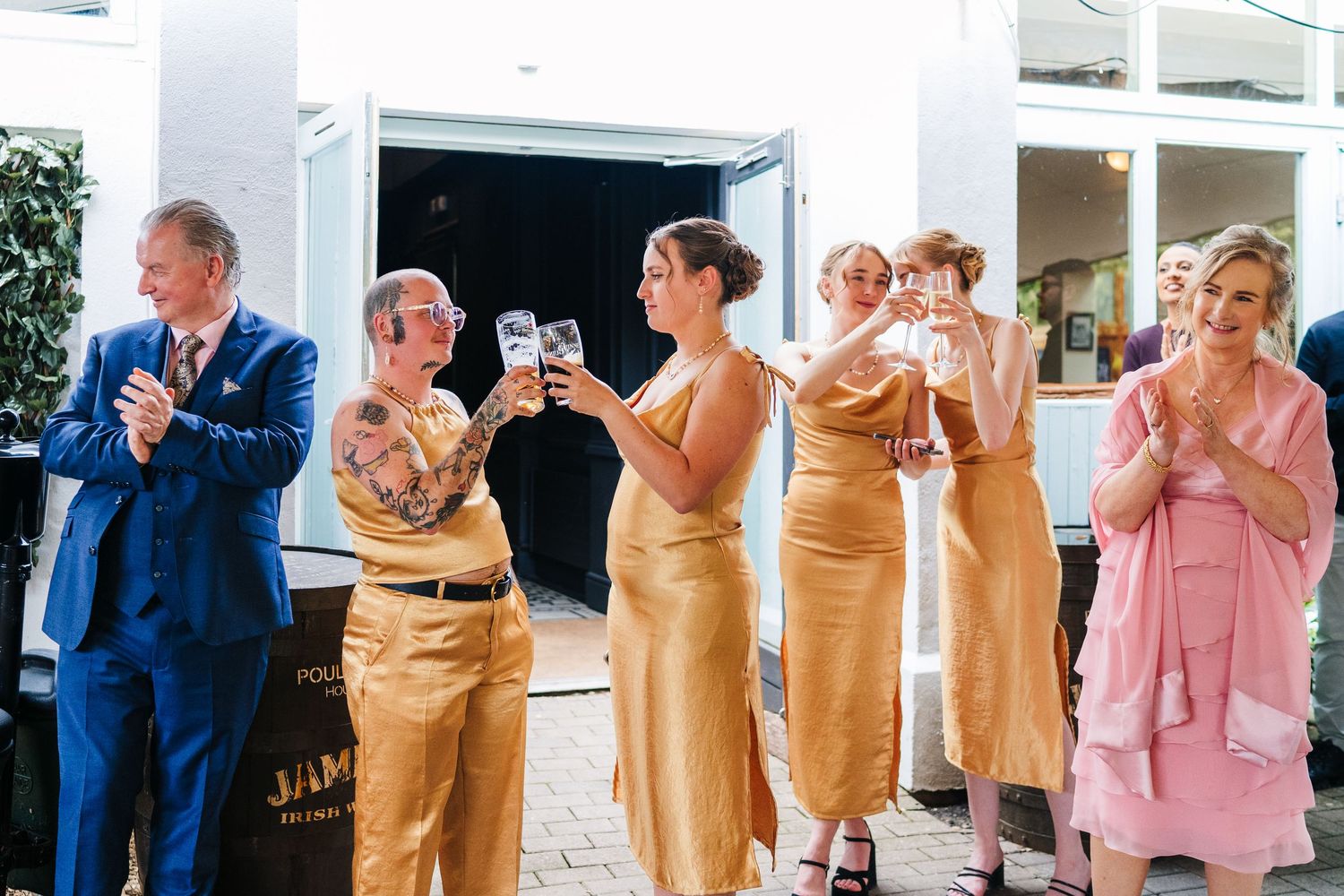 Poulaphouca Wedding photographer wicklow  Wedding party members in blue suits and gold dresses holding drinks during reception.