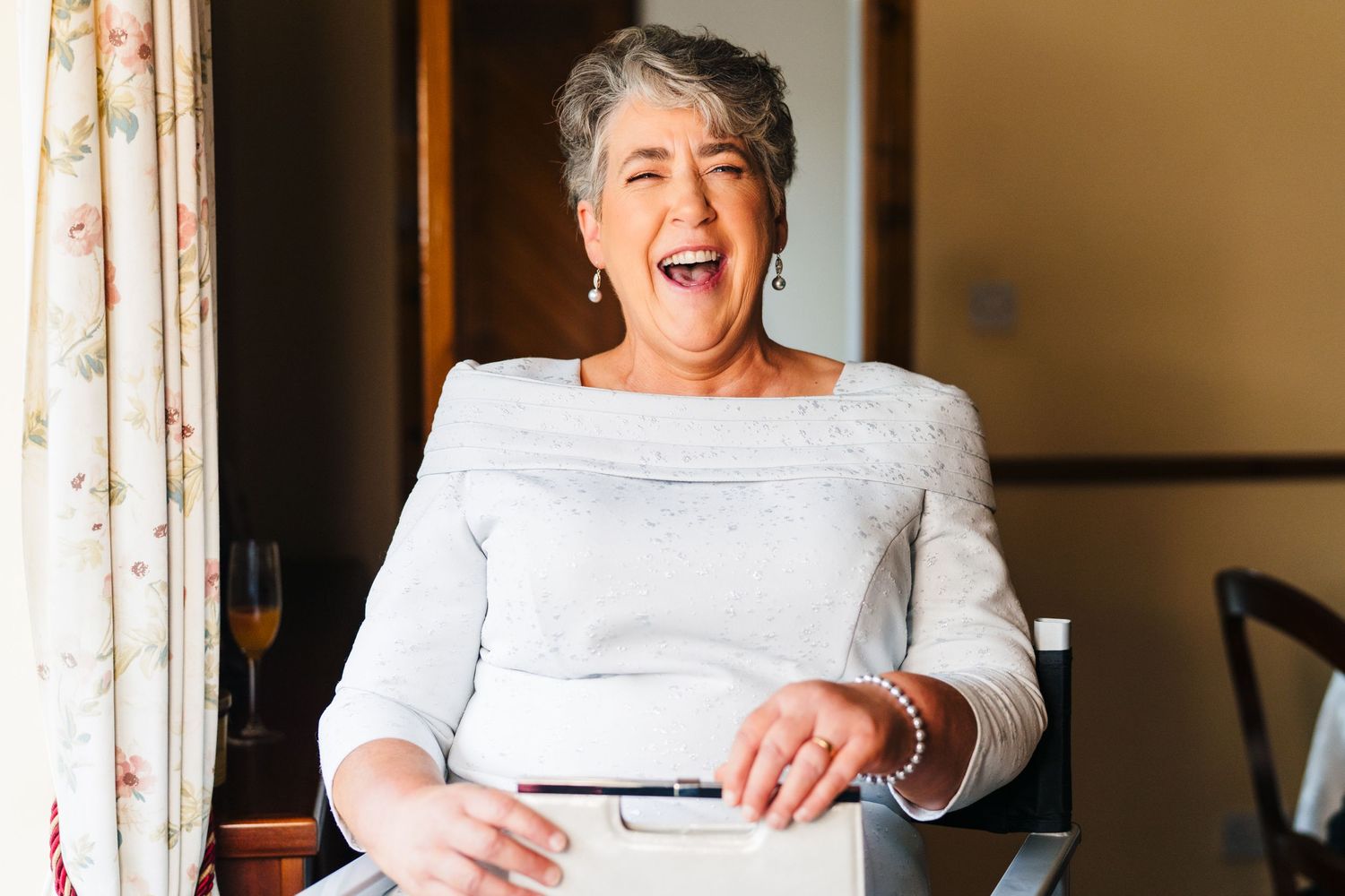 A joyful moment captured as someone in a white top sits at a table and laughs heartily near a window.Millhouse slane wedding photographer du