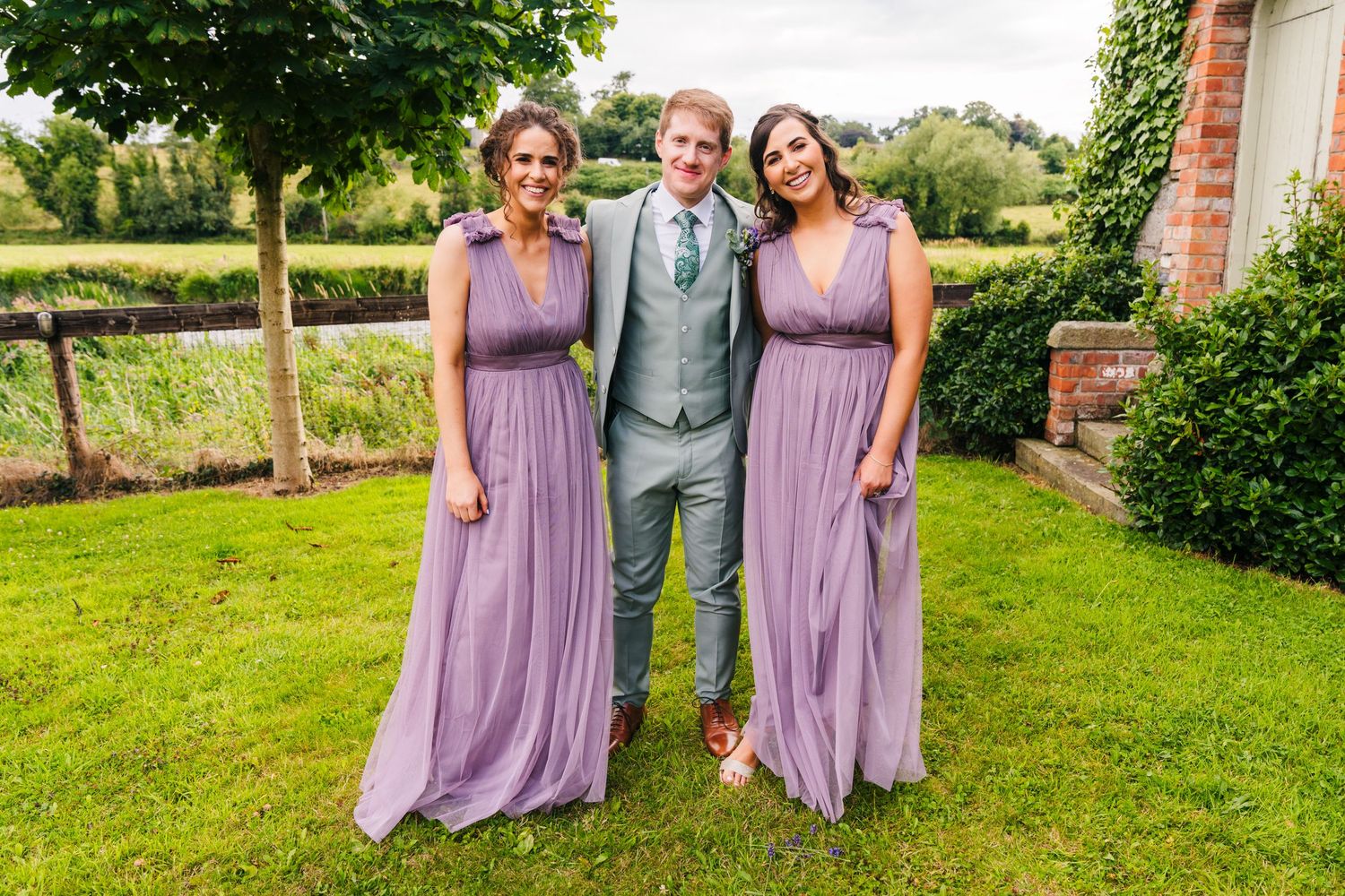 Millhouse slane wedding photographer dublin Wedding party in gray suits and lavender dresses posing on green lawn.
