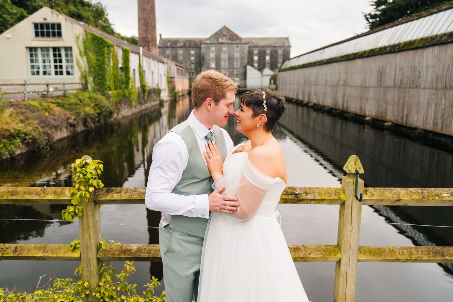 Millhouse slane wedding photographer dublin A wedding couple embrace on a rustic bridge over a scenic canal.