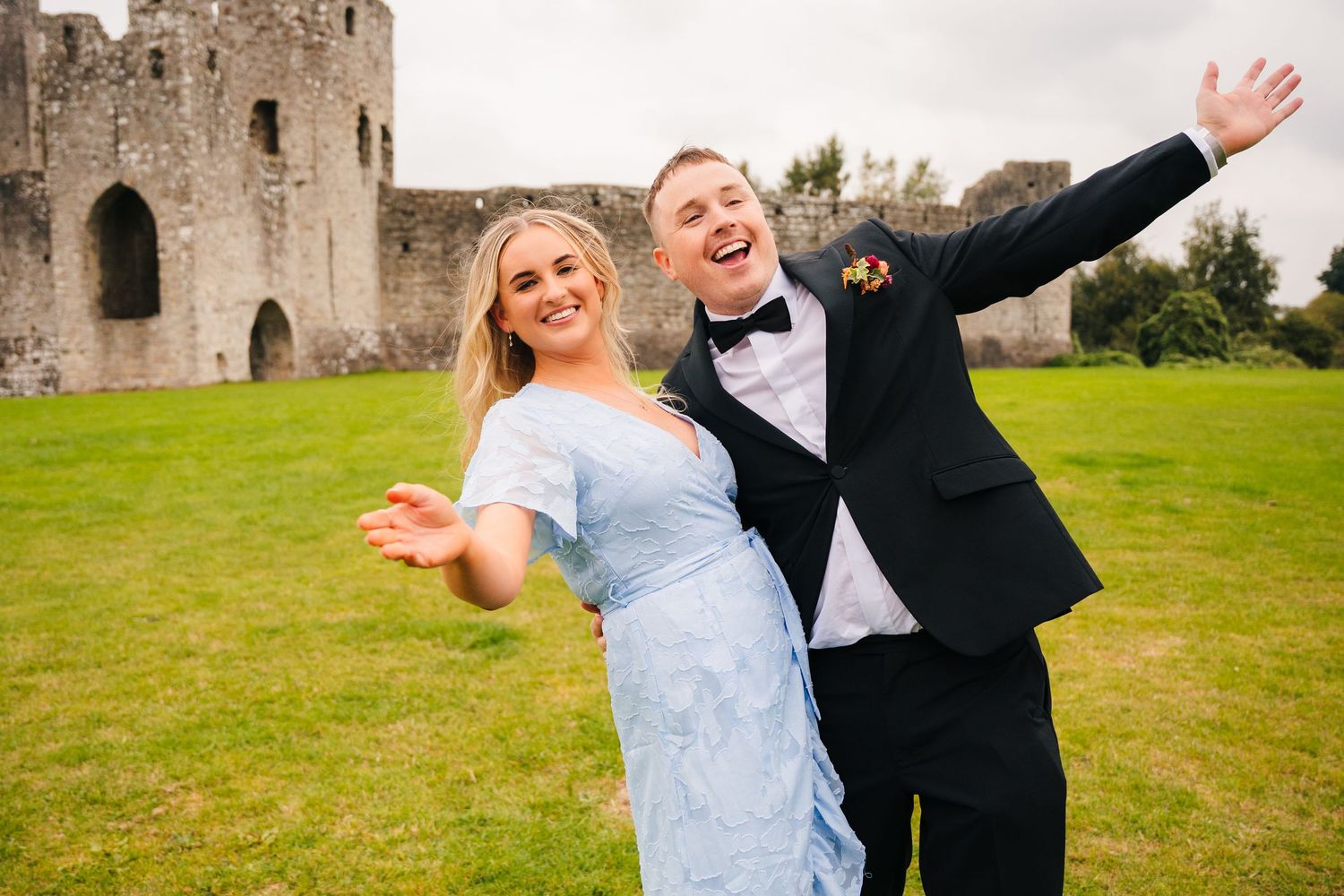 A couple strikes a joyful pose on the lawn in front of a historic castle. Wedding Photography Trim Castle Ireland