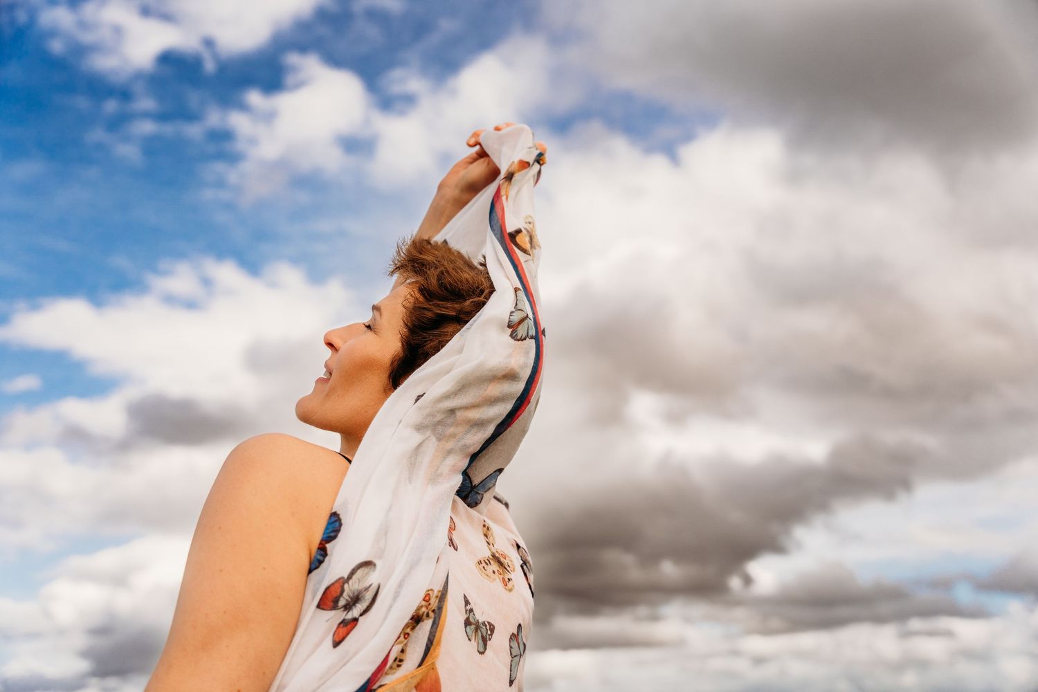 A figure twirls gracefully against a dramatic sky with white clouds and blue backdrop. Portrait PHOTOGRAPHER Dublin