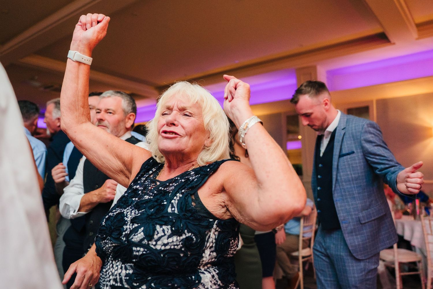 Woman in dark patterned dress dances enthusiastically at wedding reception. Portmarnock Hotel Wedding PHOTOGRAPHER Dublin