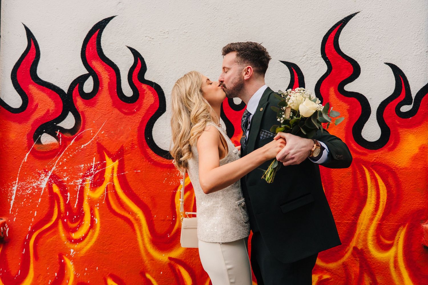 A couple poses against a vibrant red wall with painted flames, creating a dramatic wedding photo. City Hall Dublin wedding photogrAPher